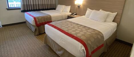 A hotel room with two beds, a window with curtains, a wall-mounted lamp, and a patterned floor.