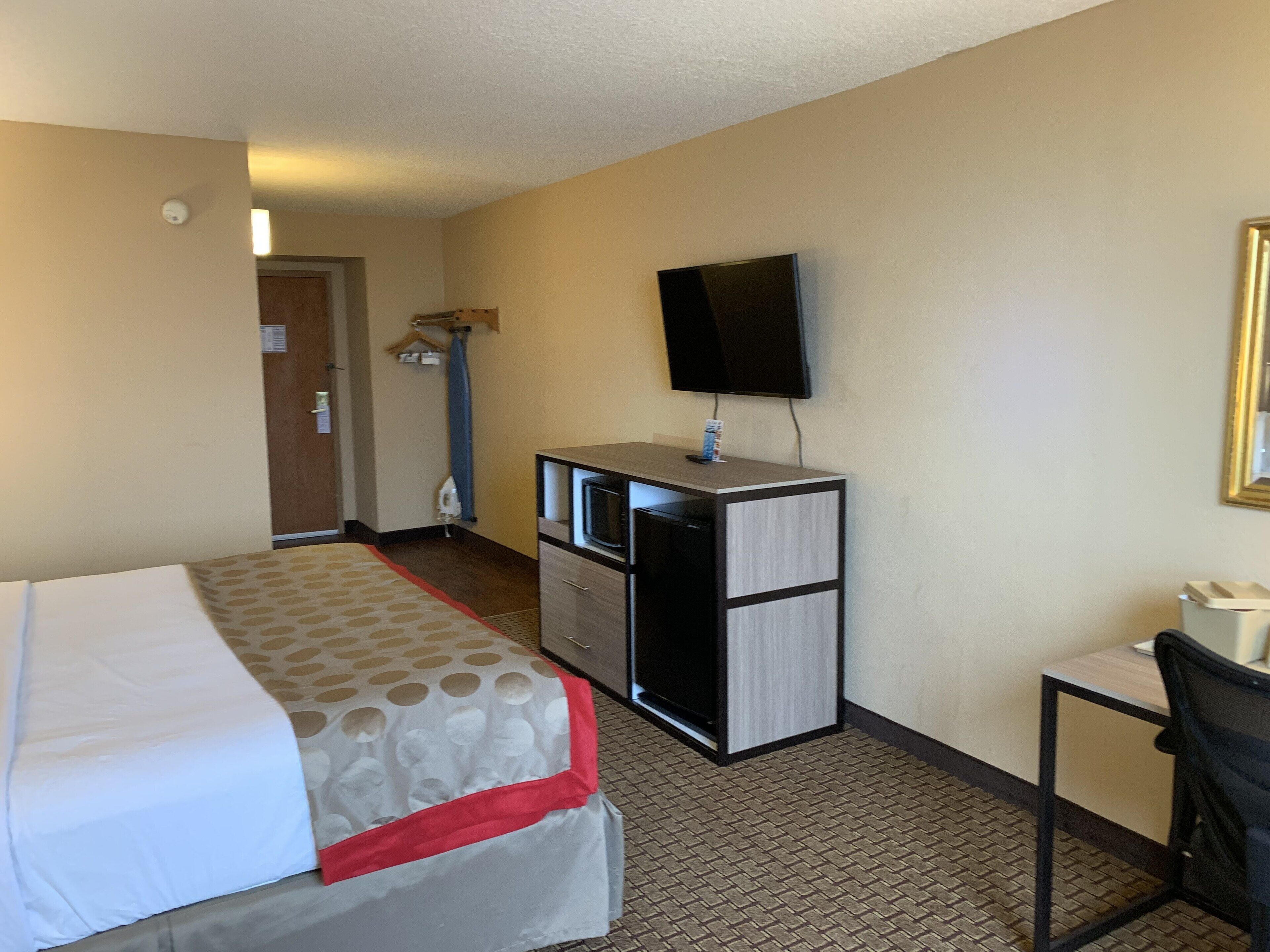 Quarto de hotel com uma cama, uma escrivaninha, uma televisão e um guarda-roupa.
