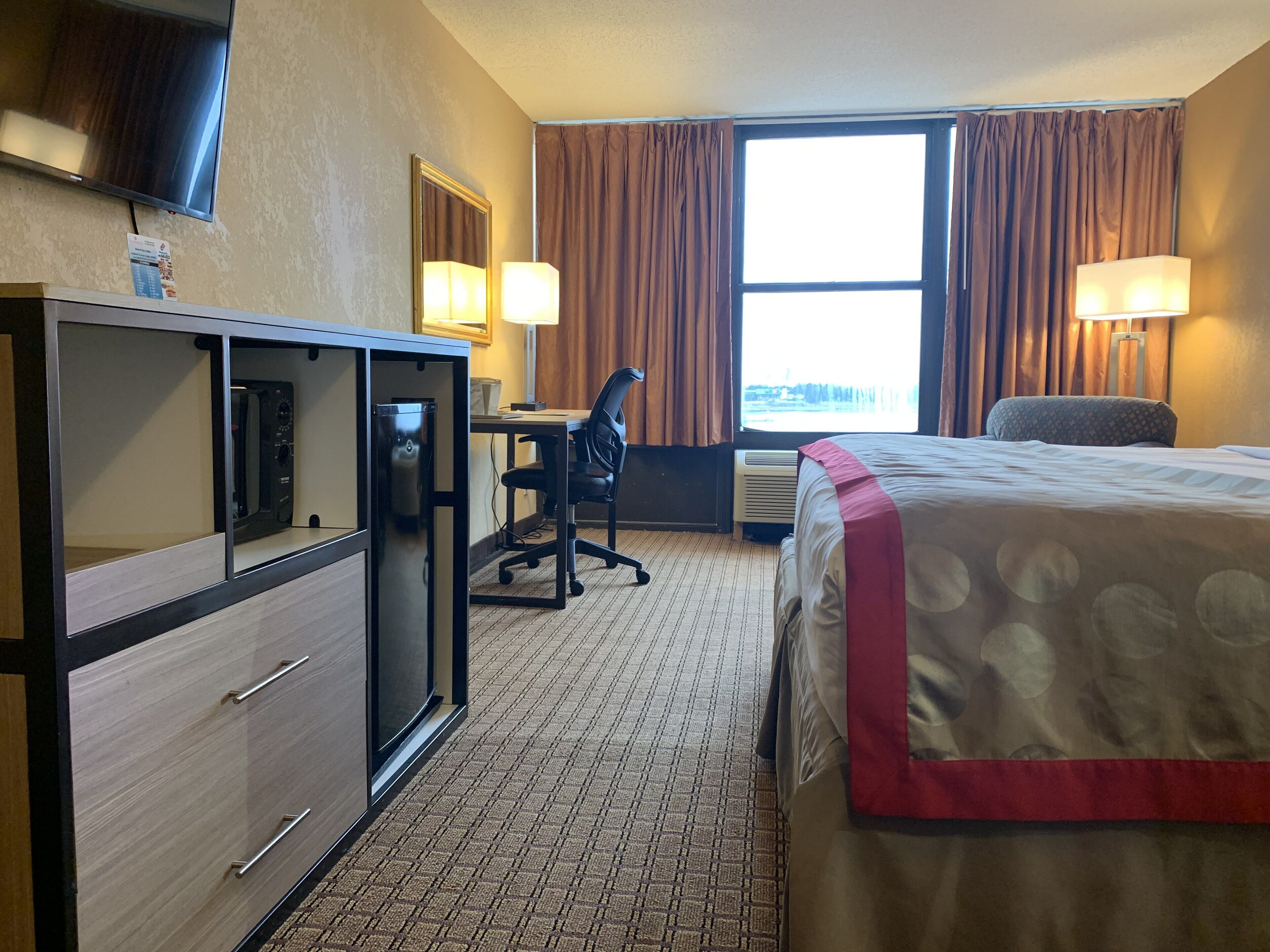 Une chambre d  ’hôtel équipée d’un lit, d’un bureau, d’une chaise et d’un téléviseur fixé au mur.