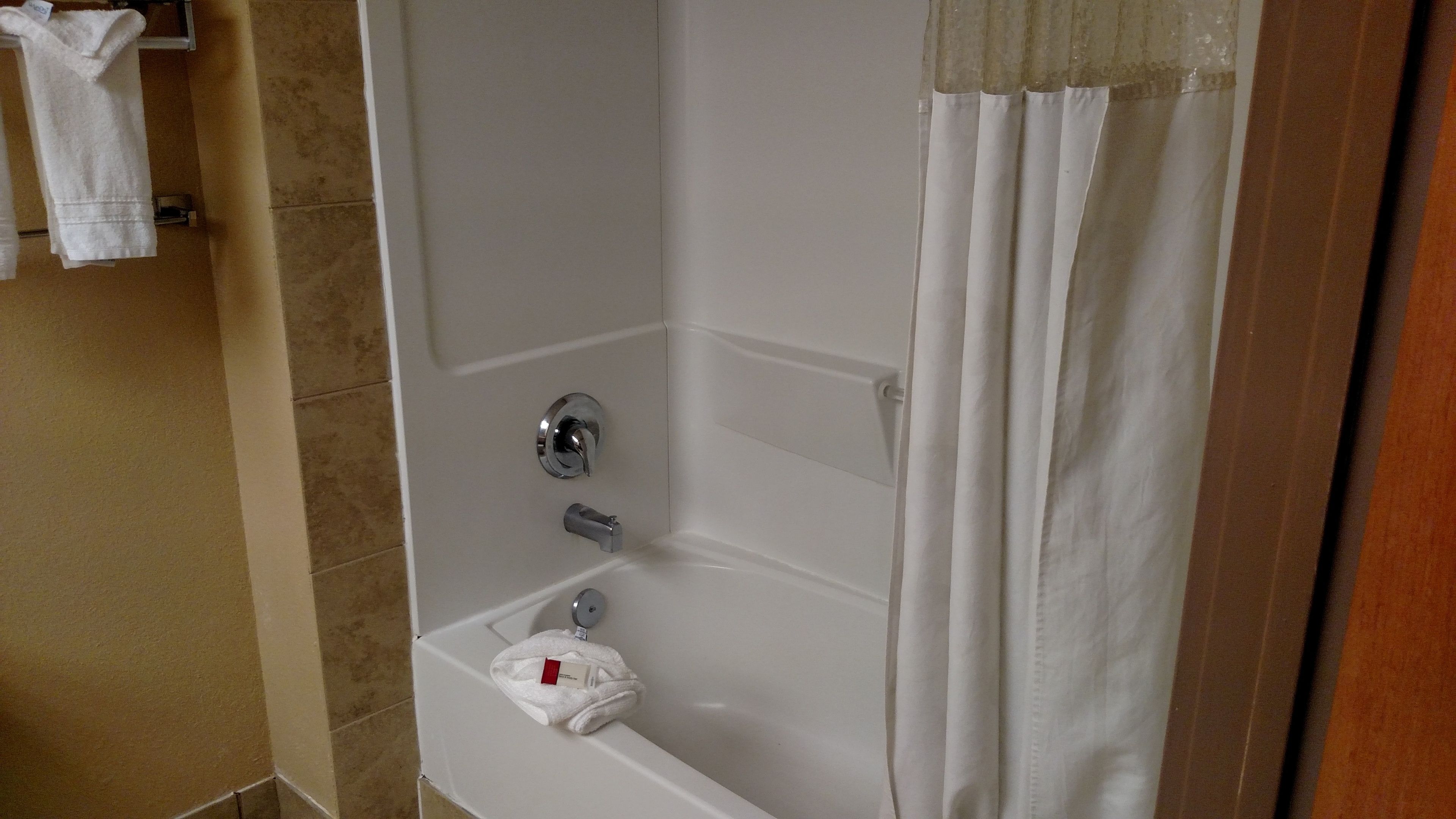A bathroom with a bathtub, a shower curtain, and a towel rack with towels.
