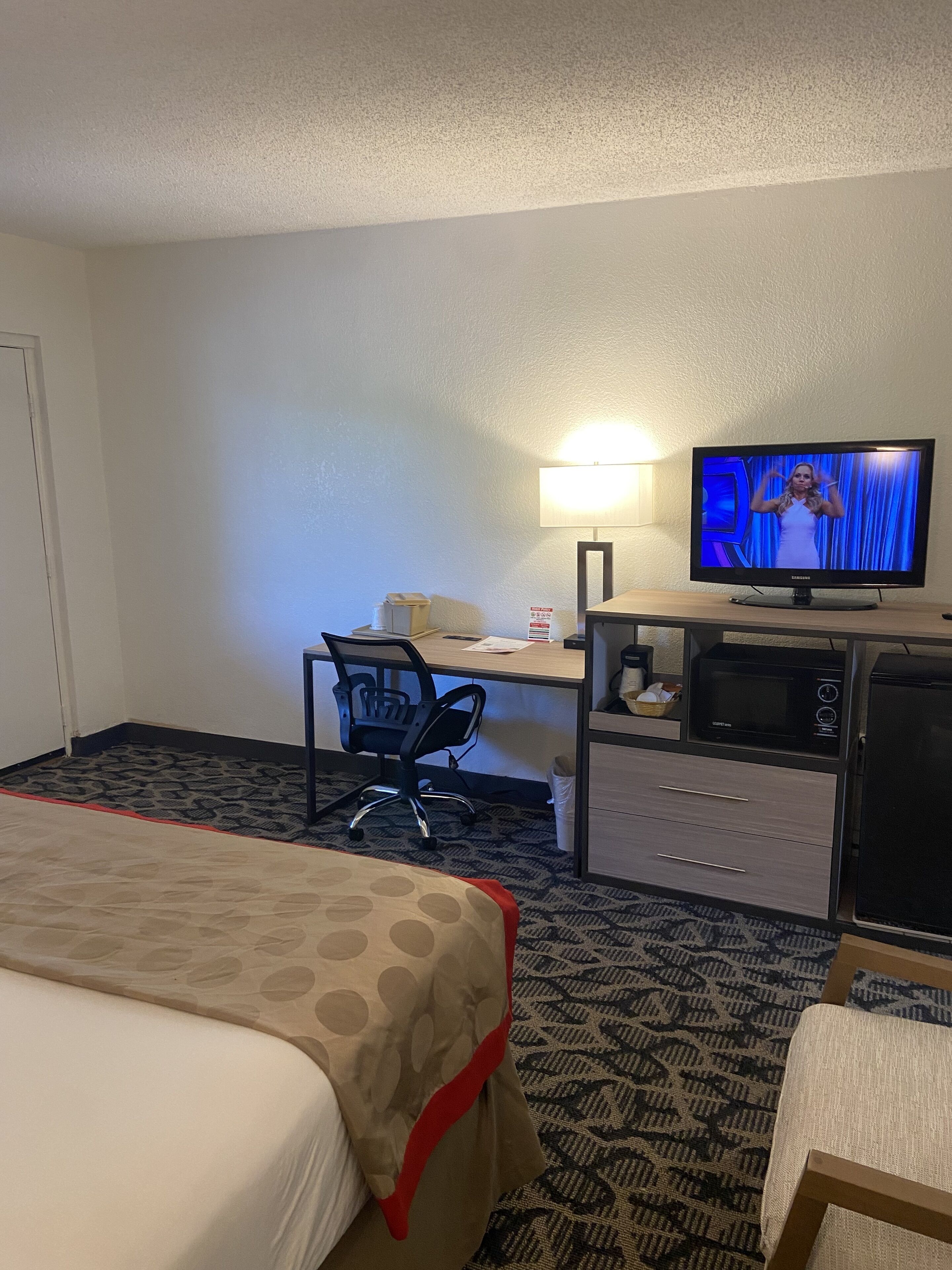Habitación de hotel con cama, escritorio con computadora, televisor, microondas y refrigerador.