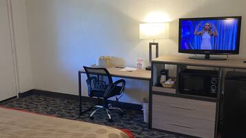 Habitación de hotel con cama, escritorio con computadora, televisor, microondas y refrigerador.