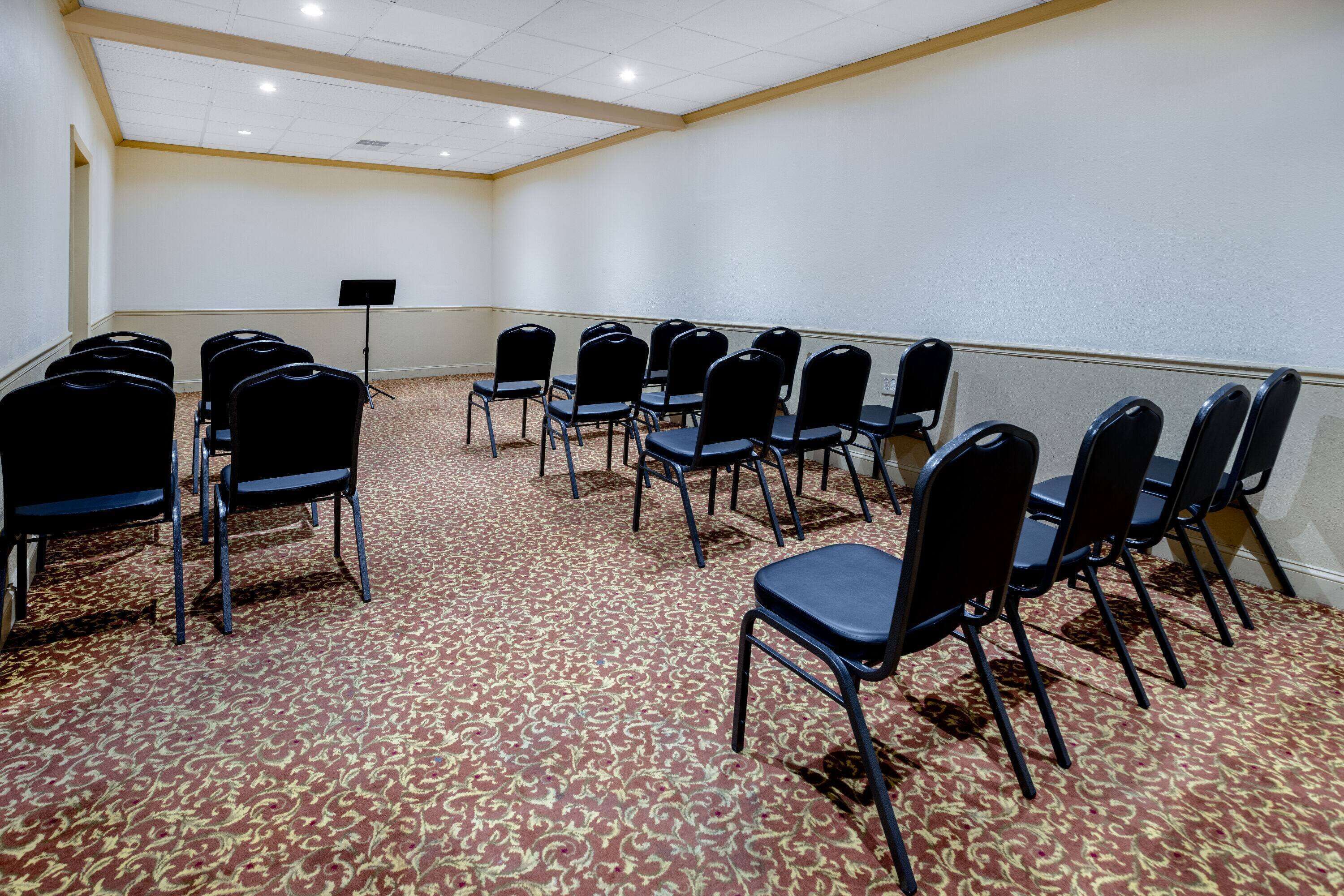 A conference room with rows of black chairs, a podium, and a carpeted floor.