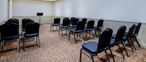 A conference room with rows of black chairs, a podium, and a carpeted floor.