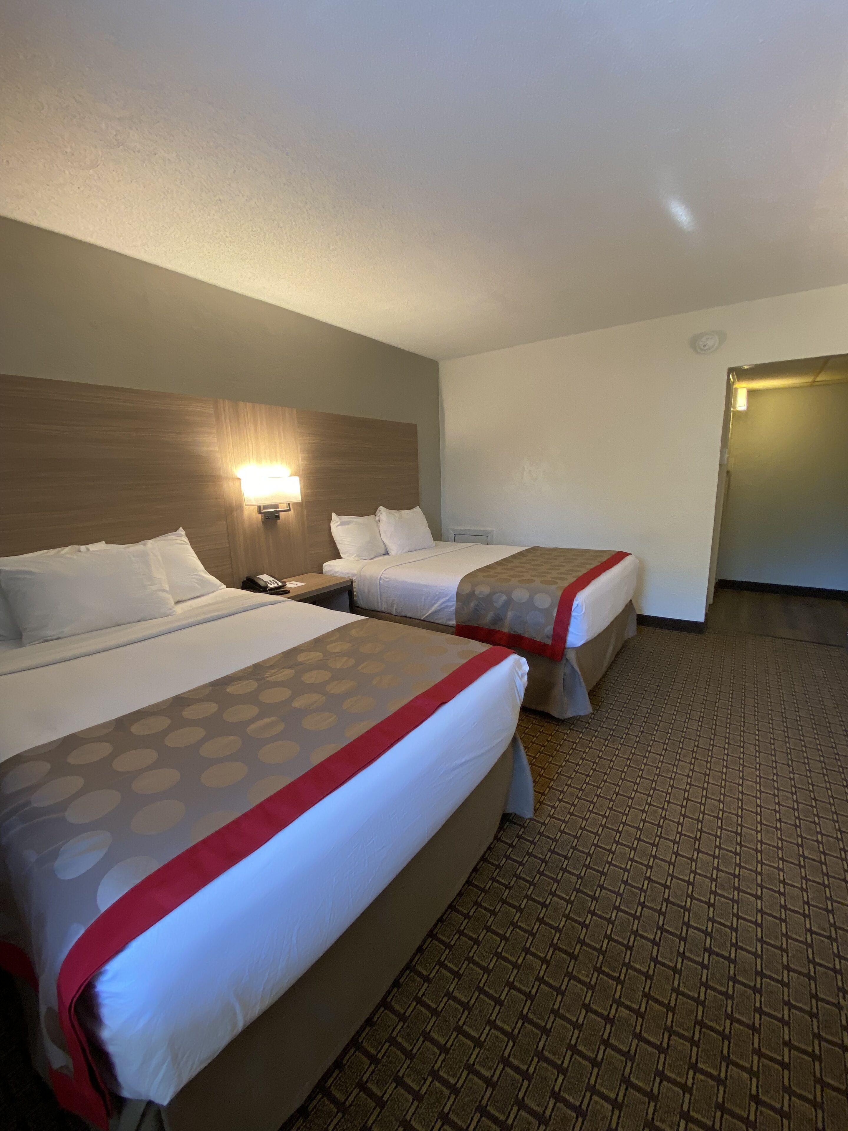 A hotel room with two beds, a nightstand, a wall-mounted lamp, and a tiled floor.