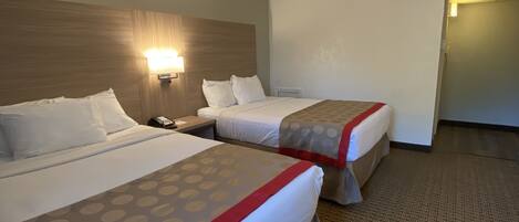 A hotel room with two beds, a nightstand, a wall-mounted lamp, and a tiled floor.