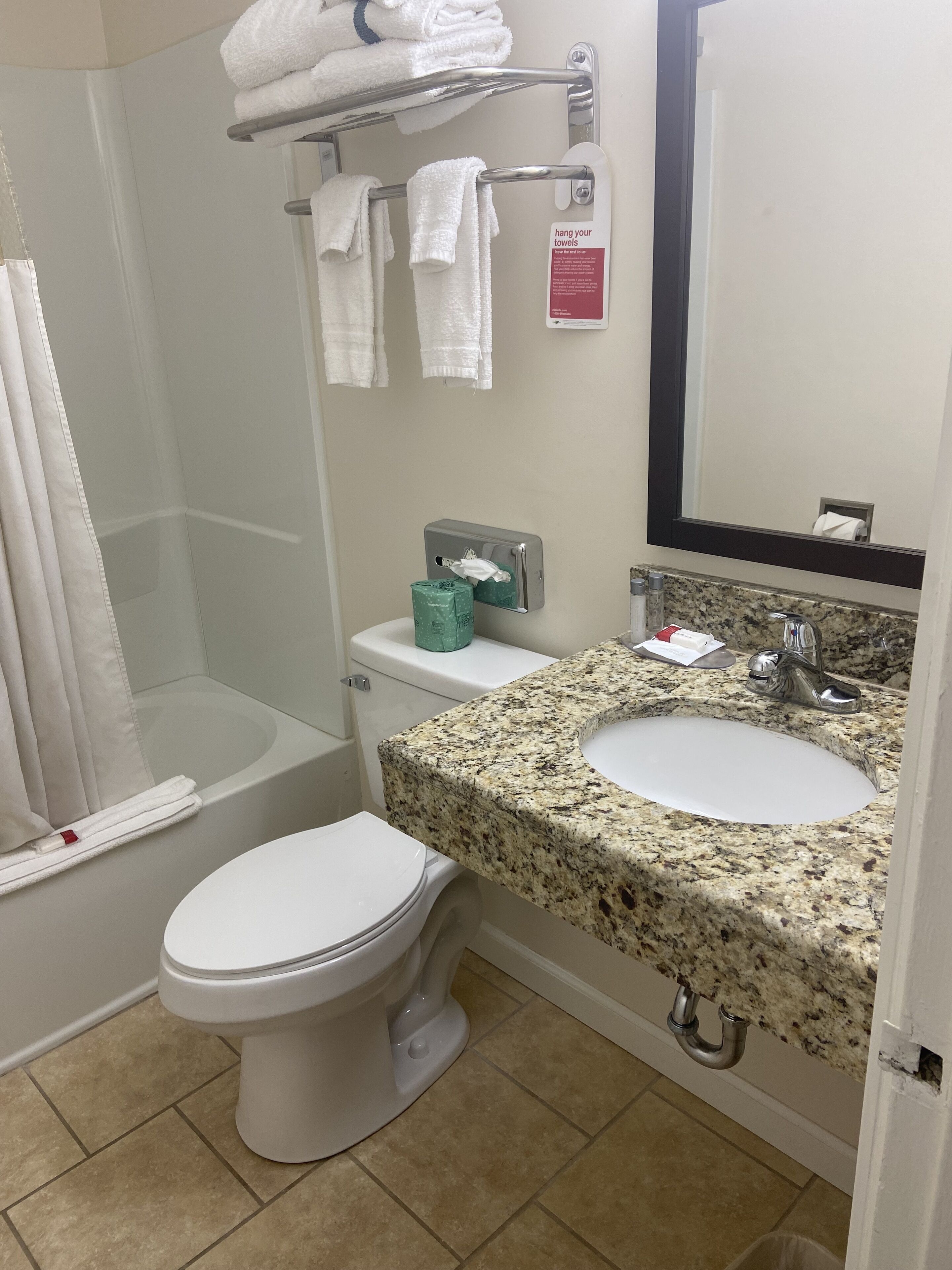 A bathroom with a toilet, sink, and shower. There are towels on a rack and a sign instructing to hang towels.