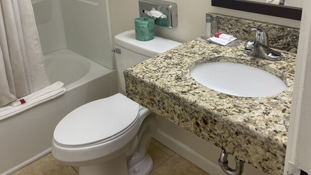 A bathroom with a toilet, sink, and shower. There are towels on a rack and a sign instructing to hang towels. - Ramada by Wyndham West Atlantic City (Pleasantville)