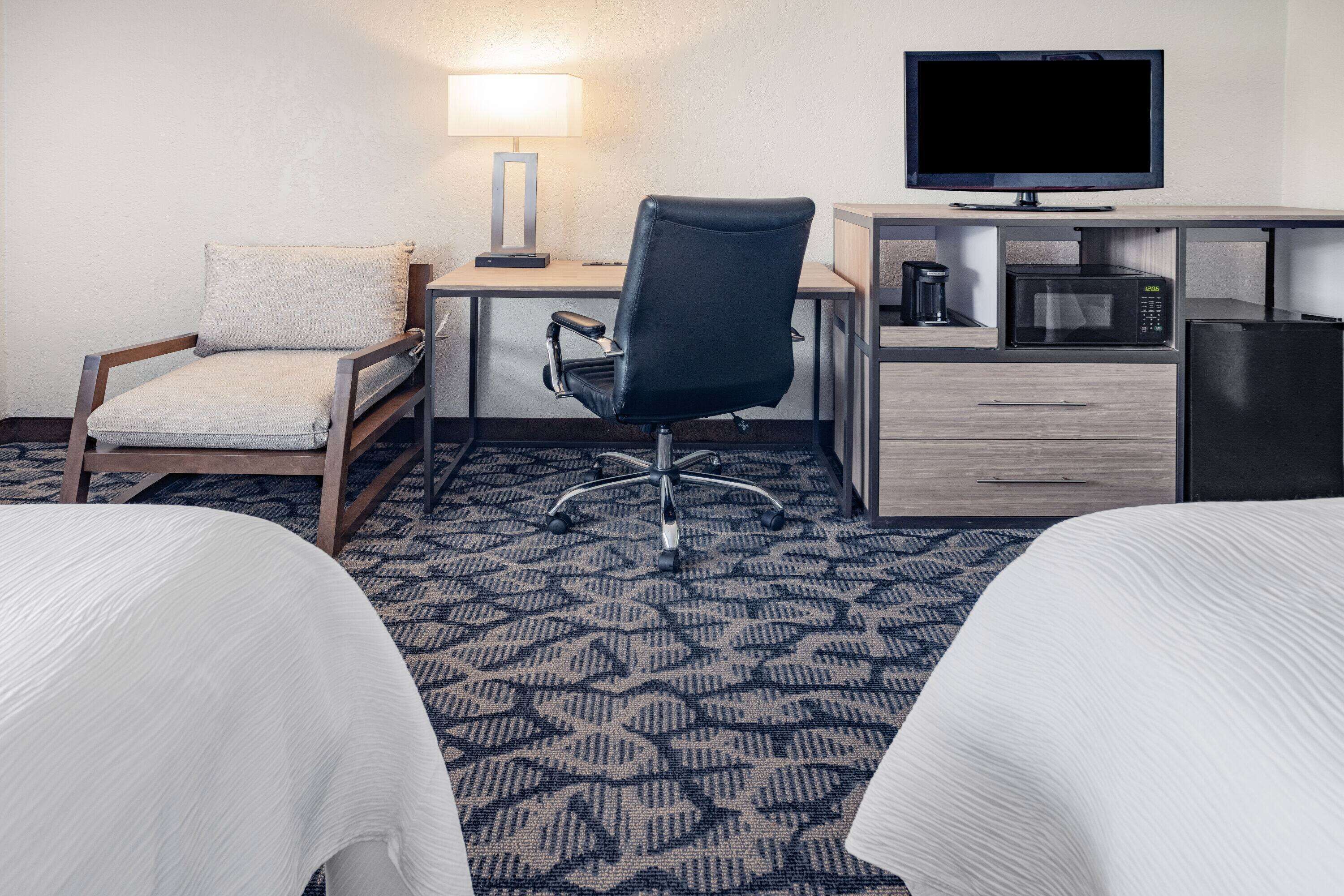 Ein Hotelzimmer mit Schreibtisch, Stuhl, Fernseher, Mikrowelle und zwei Betten.