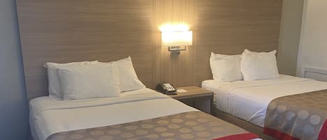 Una habitación de hotel con dos camas, una mesita de noche con un teléfono y una lámpara de pared.