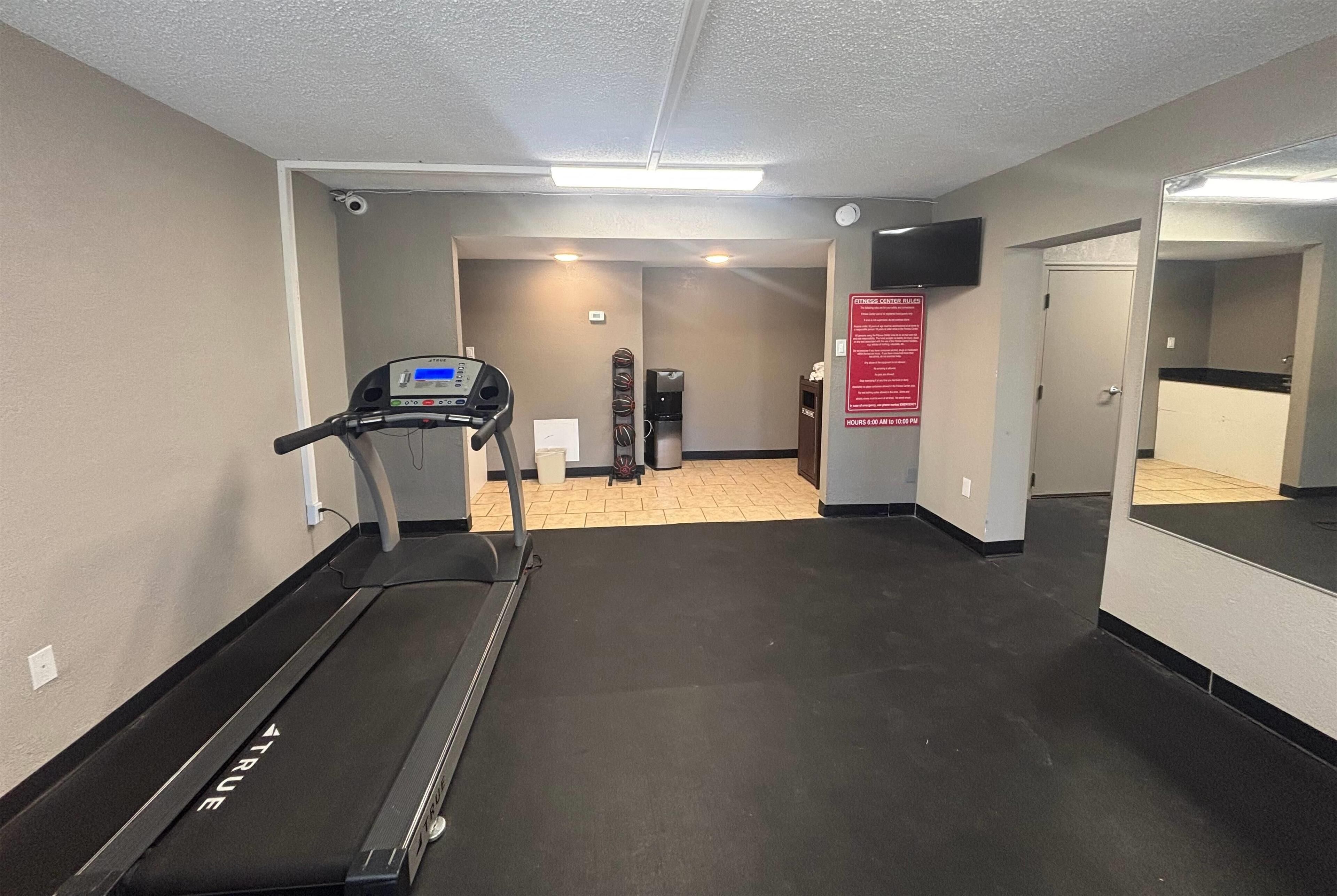 A fitness center with treadmills, a wall-mounted TV, and a sign detailing the center's rules.