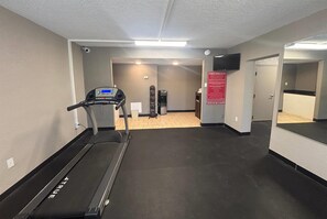 Un gimnasio con cinta de correr, dispensador de agua y letrero del centro de acondicionamiento físico.