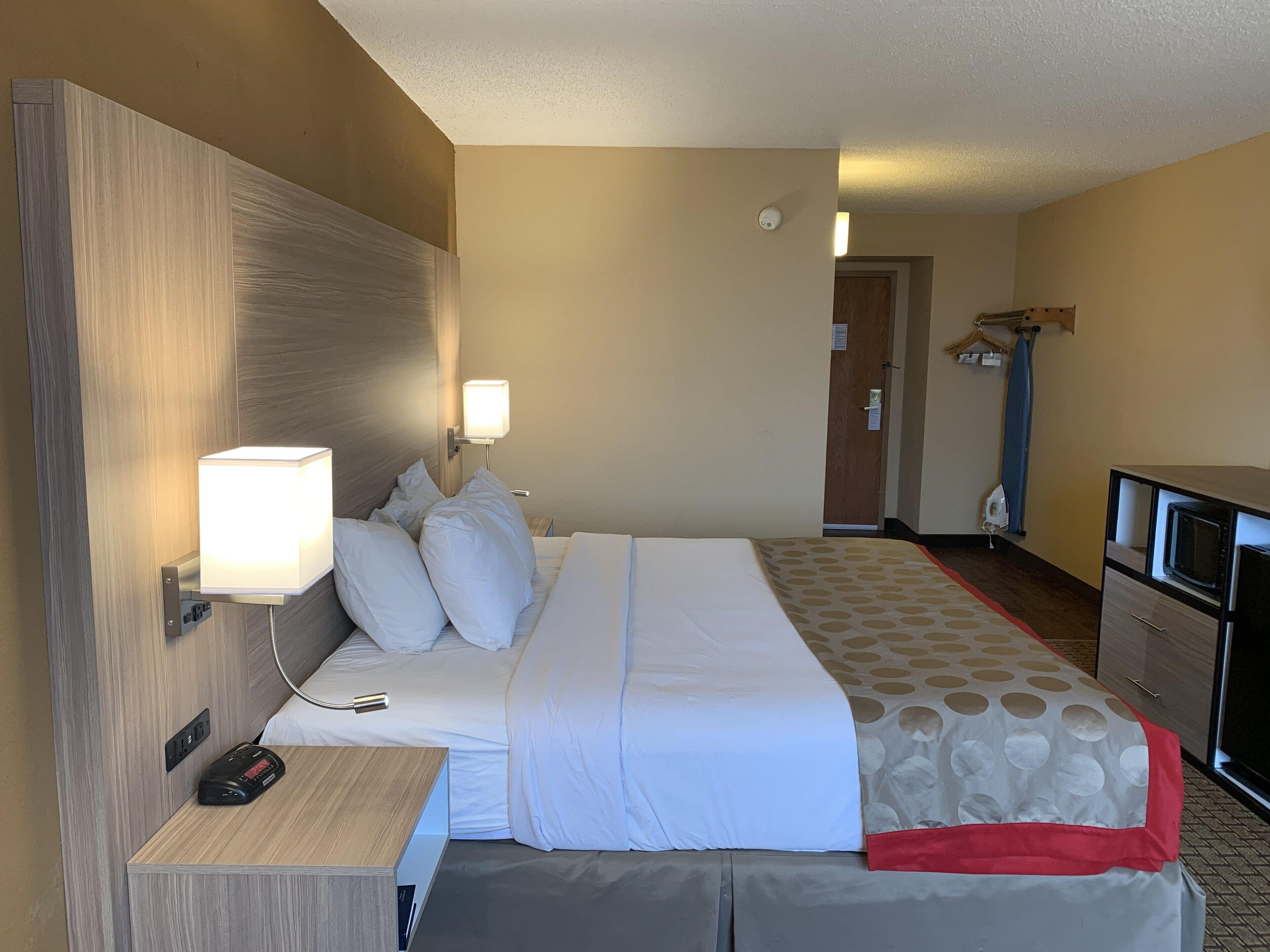 Quarto de hotel com cama, mesa de cabeceira, abajur e televisão.