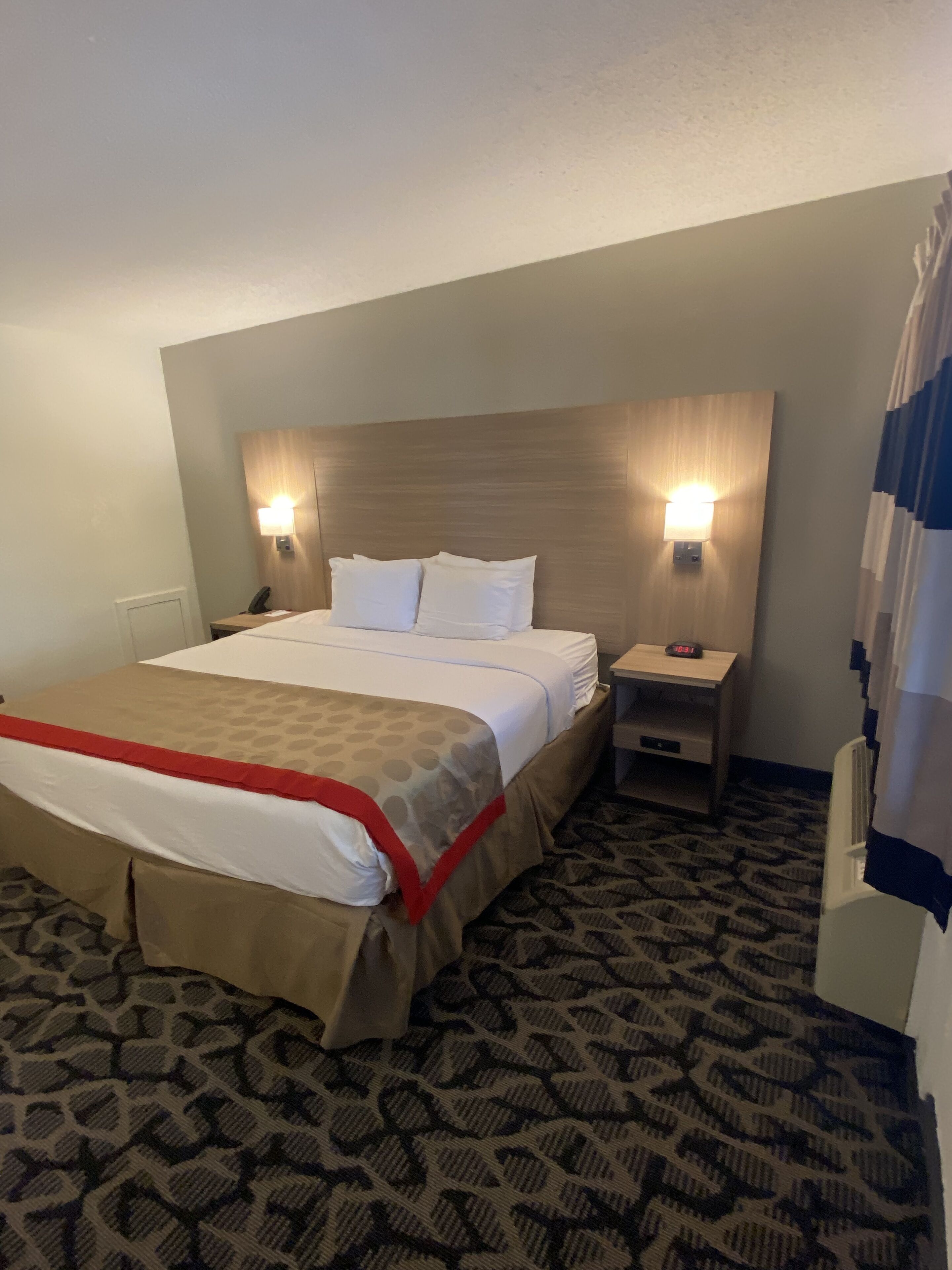 A hotel room with a bed, two bedside lamps, a nightstand, and a clock.