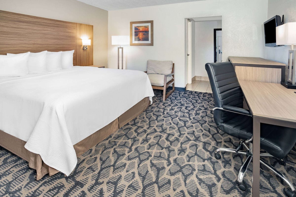 A hotel room with a large bed, a desk with a chair, a lamp, and a television.