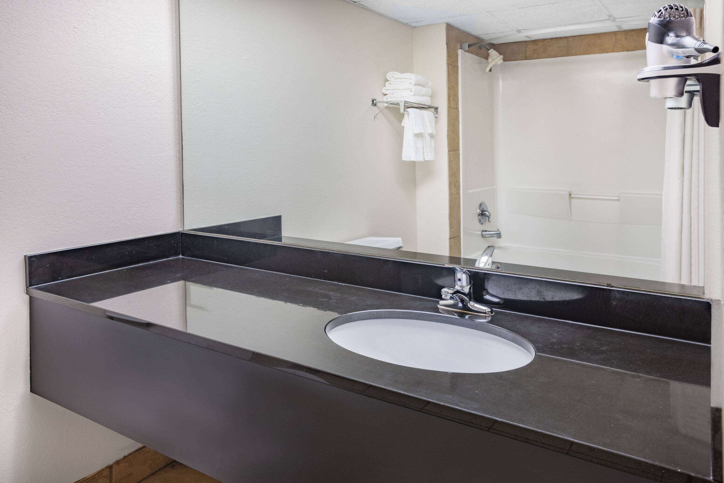 A modern bathroom with a large mirror, a black countertop, and a white sink.