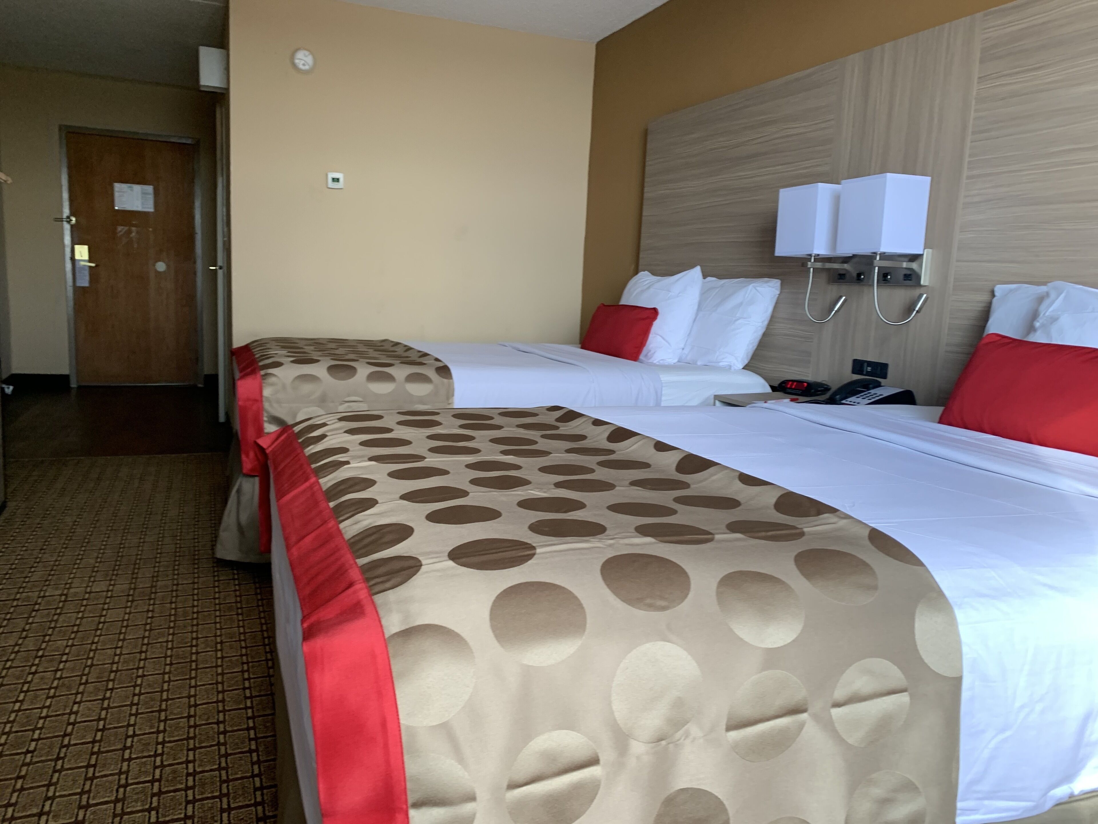 A hotel room with two beds, a wooden headboard, a clock, and a telephone.