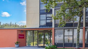 Un edificio moderno con entrada de vidrio, un letrero que dice "RAMADA" y una planta en maceta al frente.