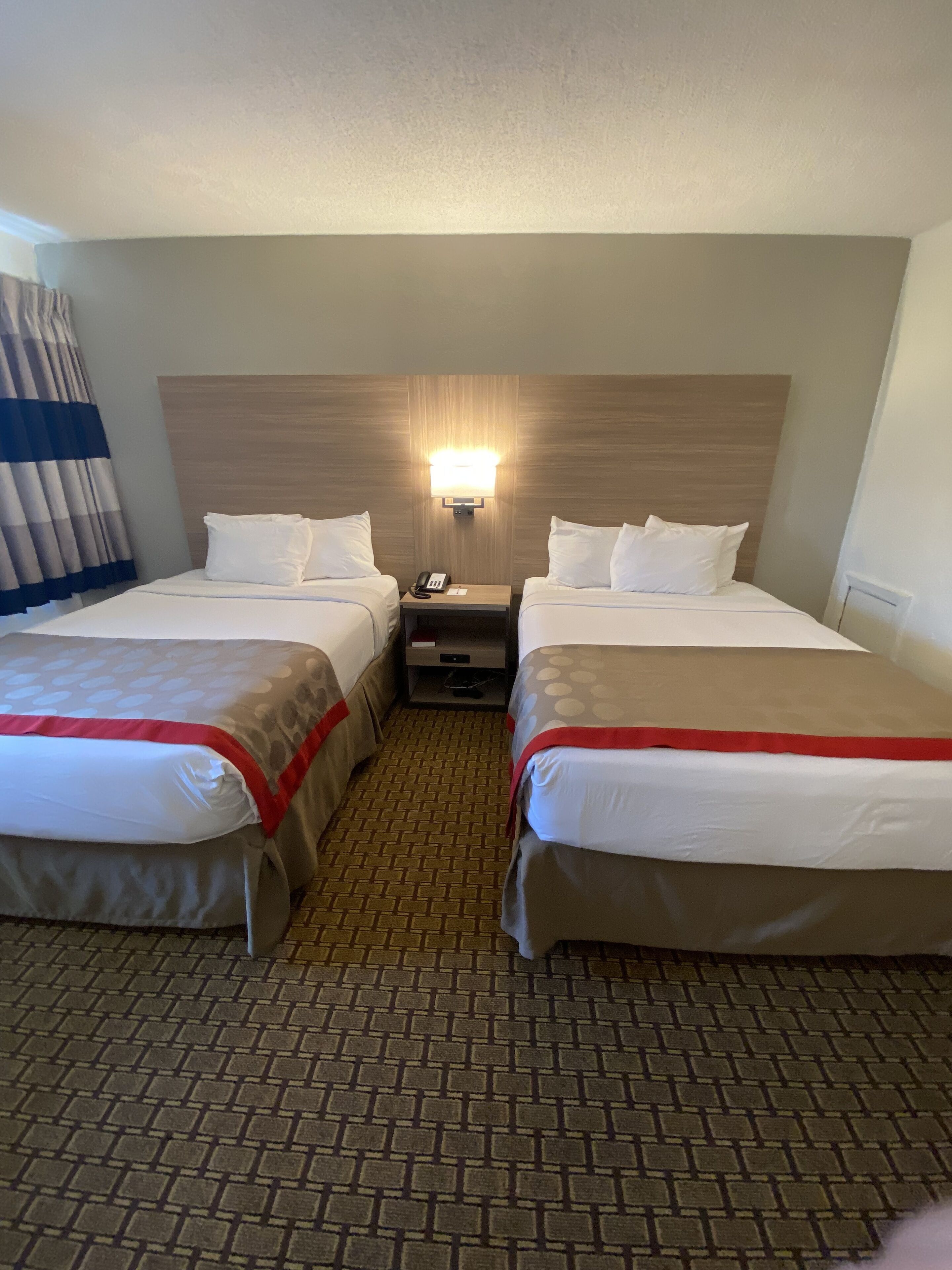 Una habitación de hotel con dos camas, una mesita de noche, una lámpara y un mostrador de recepción.