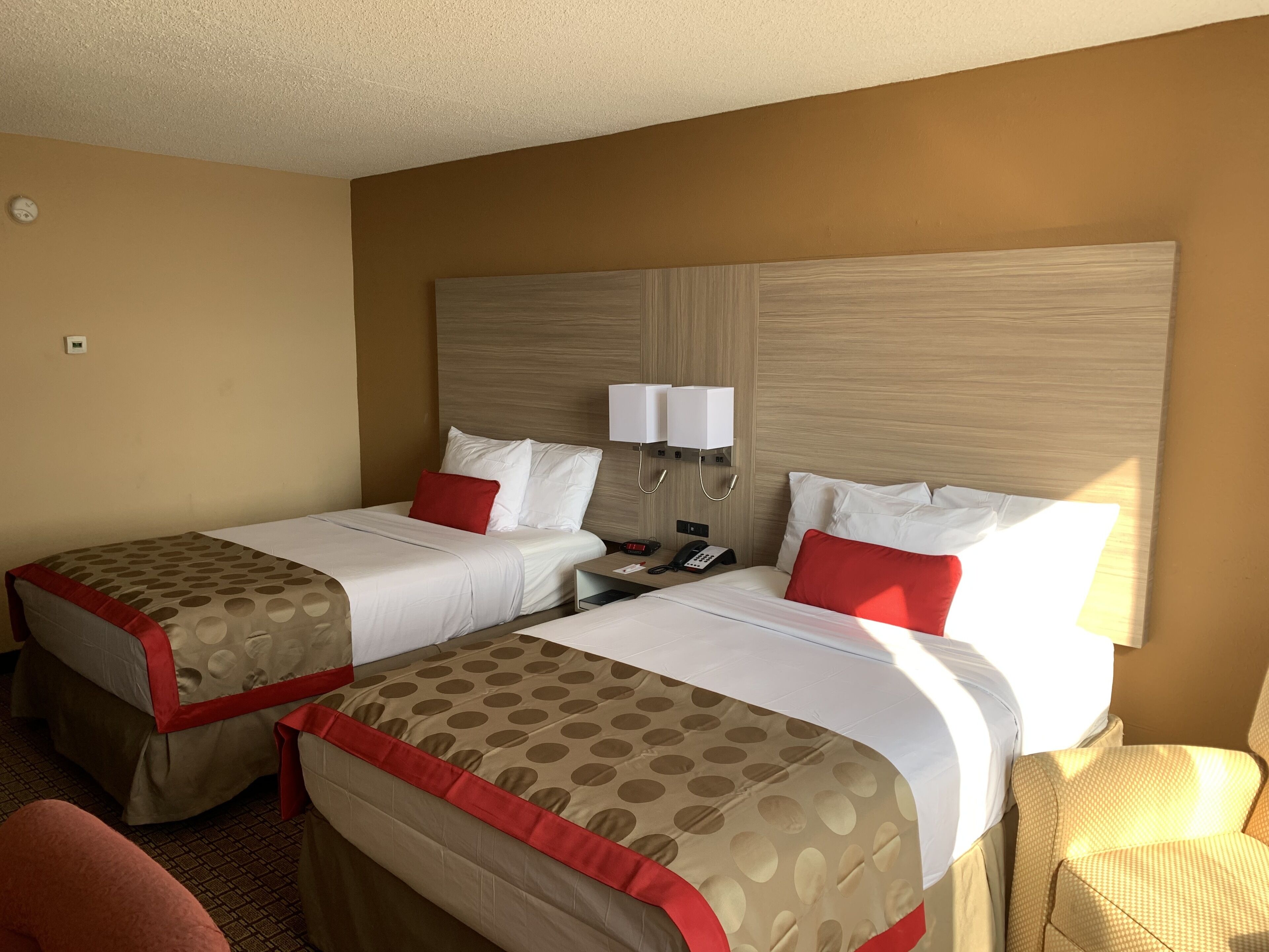 Ein Hotelzimmer mit zwei Betten, jedes mit einer roten und weißen Spitze-Bettdecke, einem Holz-Kopfteil, Nachttischlampen und einem Telefon.