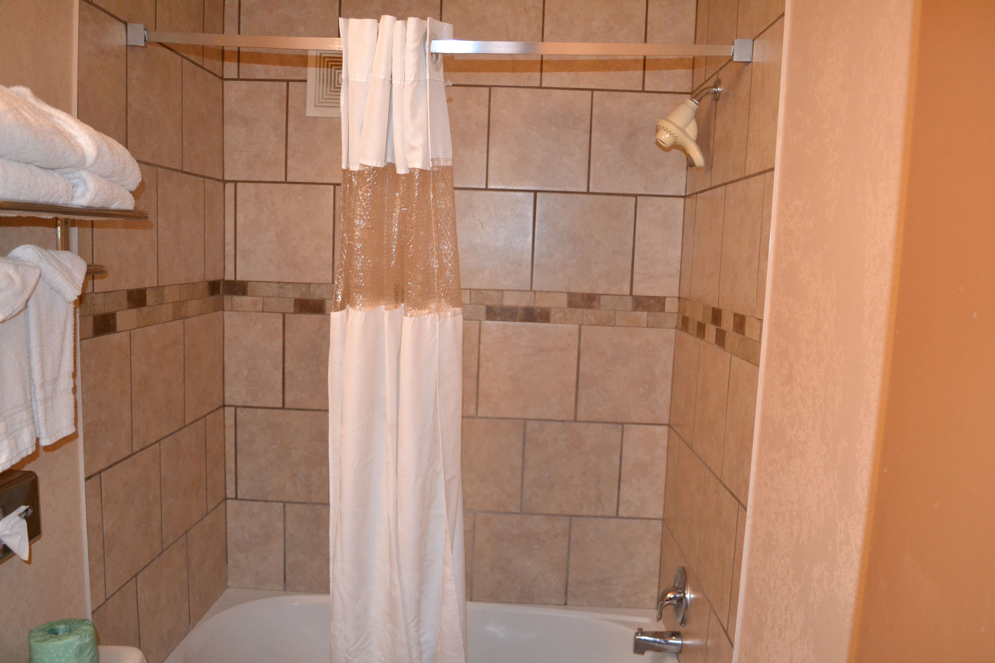 A shower area with a white curtain, tiled walls, and a visible towel rack.