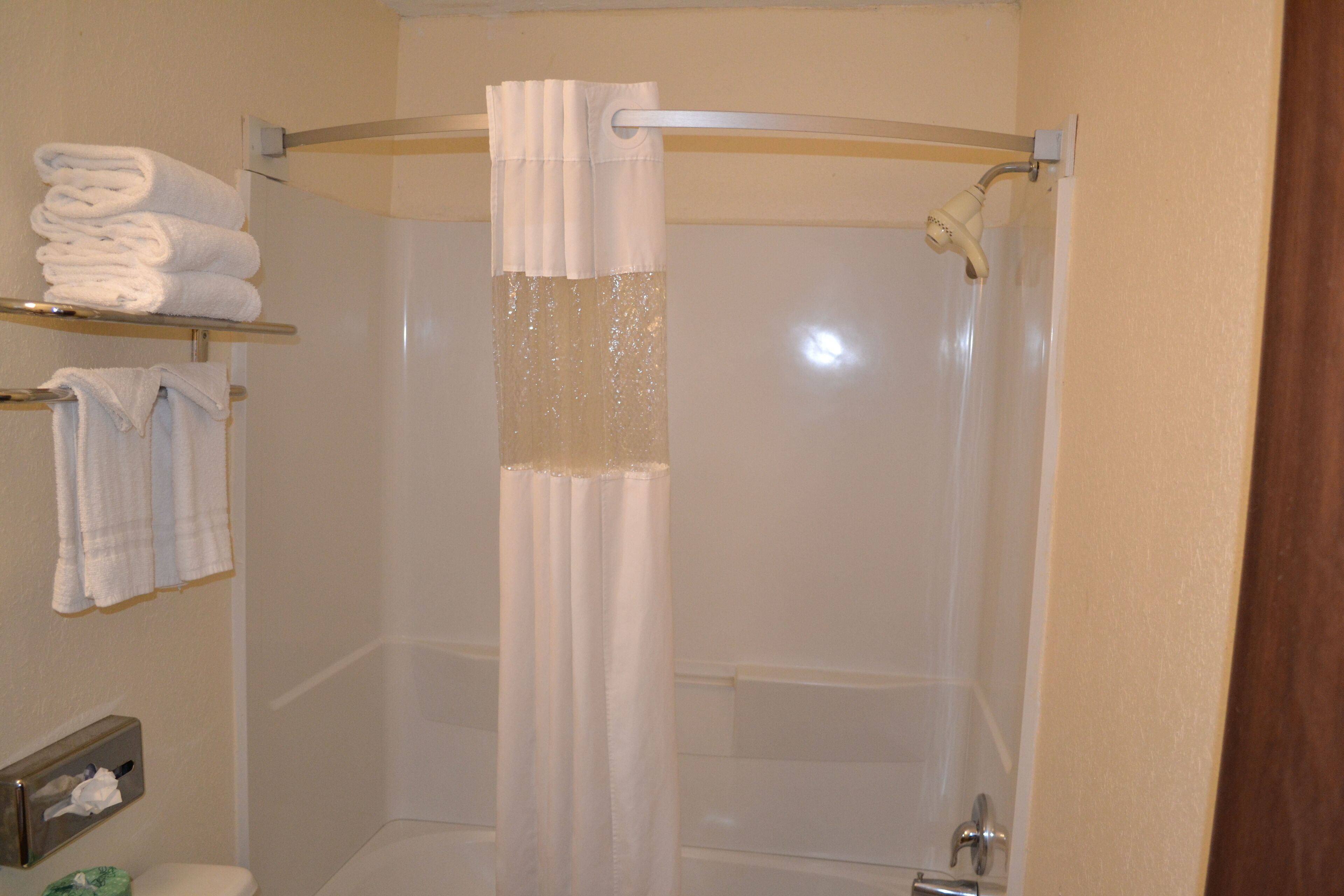 A bathroom with a shower curtain, a toilet, and a shelf with folded towels.
