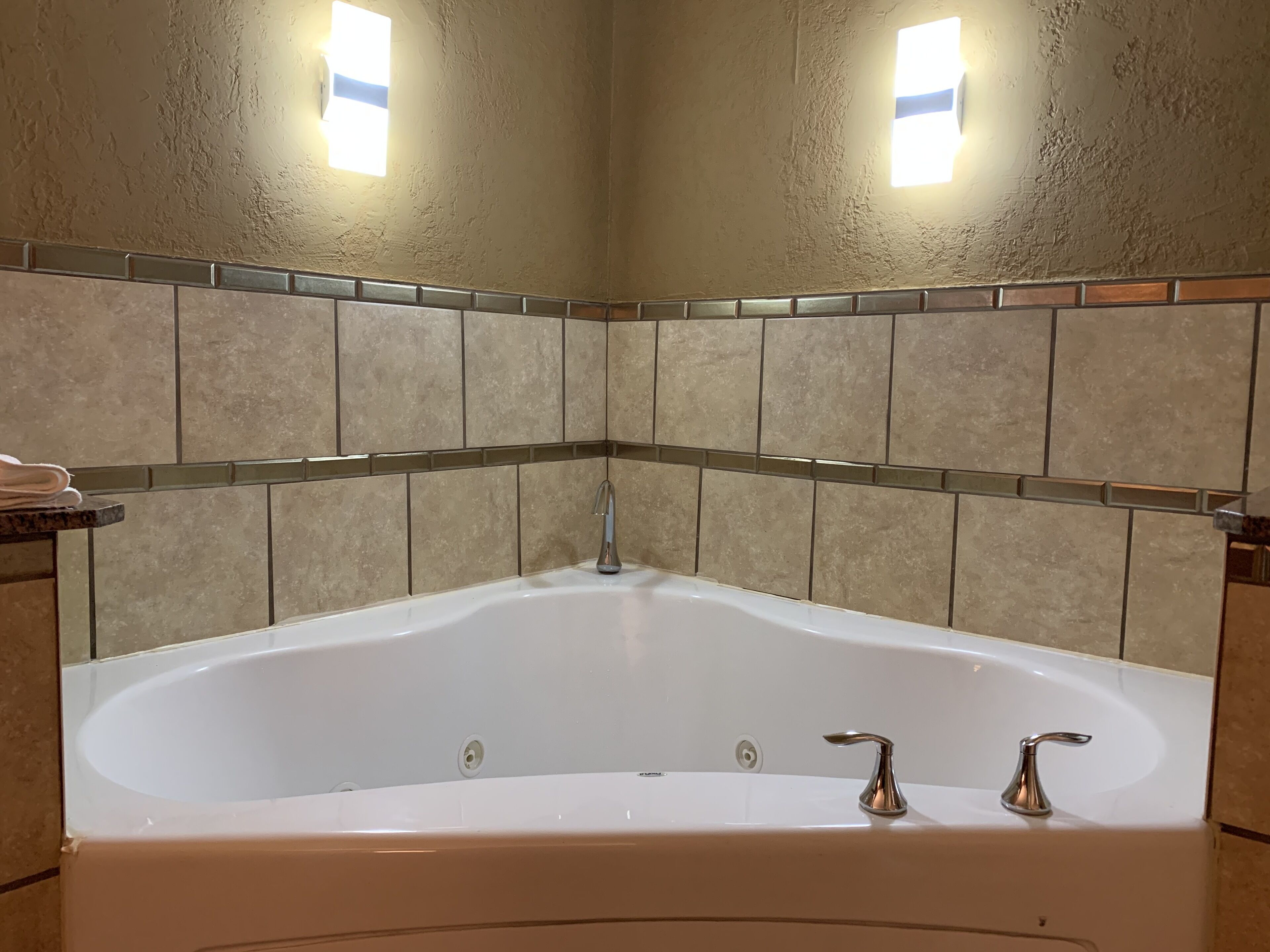 A bathroom with a freestanding bathtub, beige tiled walls, and two wall-mounted lights.