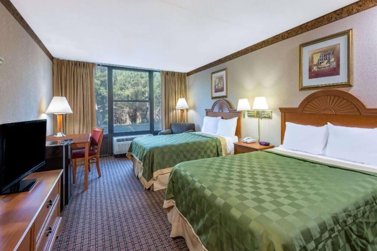 A hotel room with two beds, a desk with a TV, a chair, and a window with curtains.