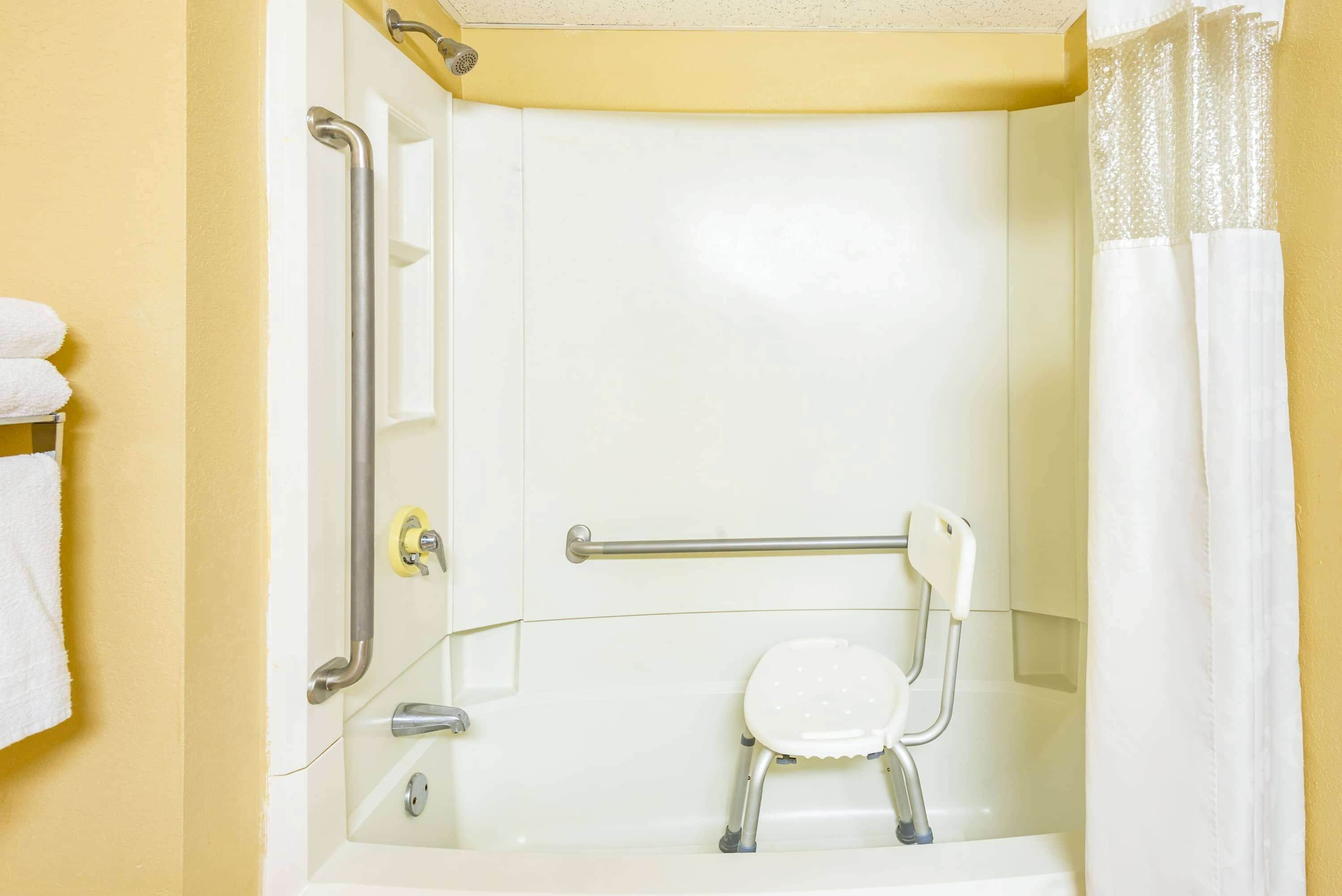 A bathroom with a bathtub, a shower chair, and a grab bar.