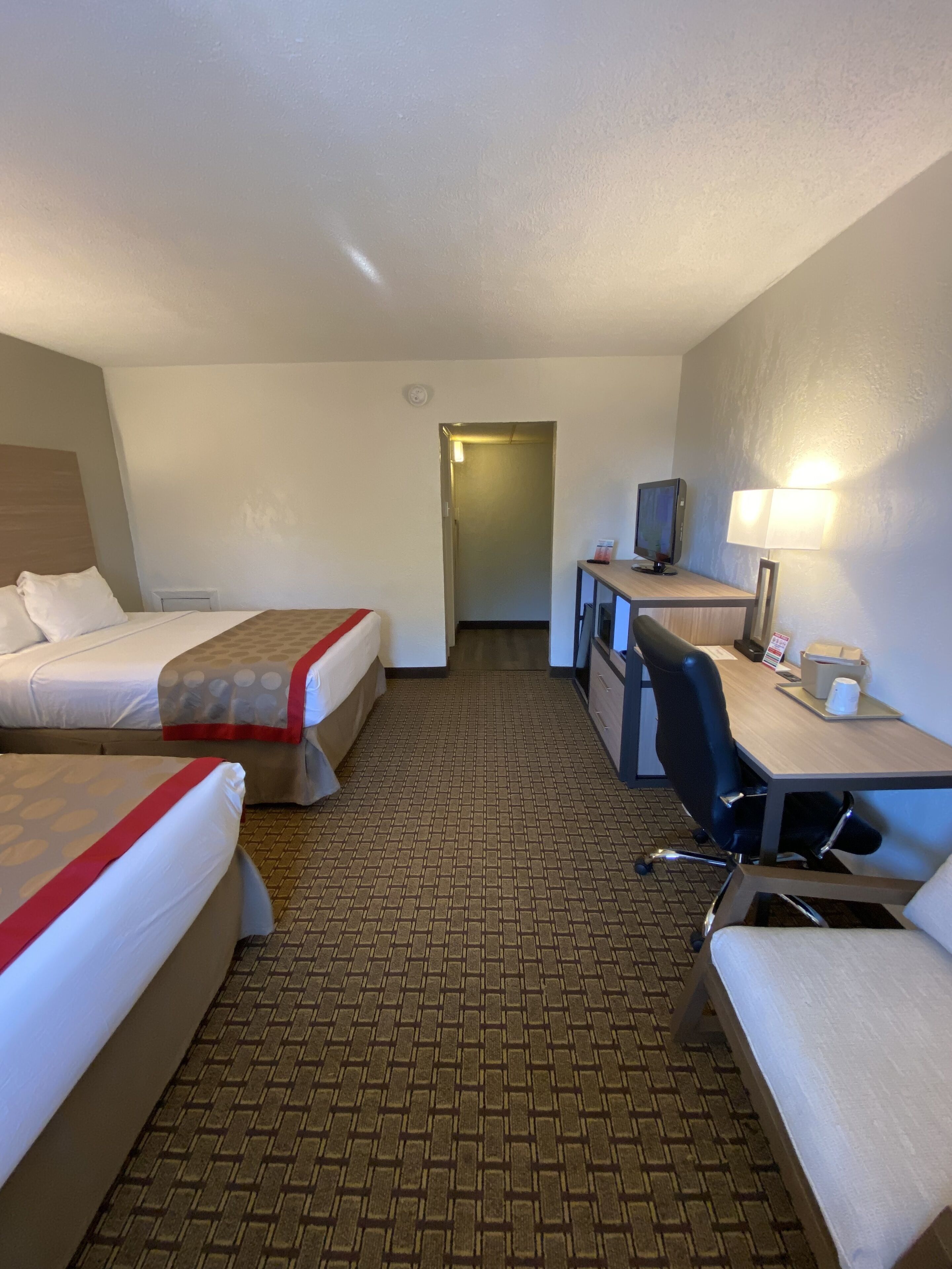 Une chambre d’hôtel avec deux lits, un bureau, une chaise, une télévision et une lampe.