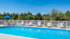 Una piscina rectangular con agua azul cristalina, rodeada por una cerca blanca y varias sillas de descanso.