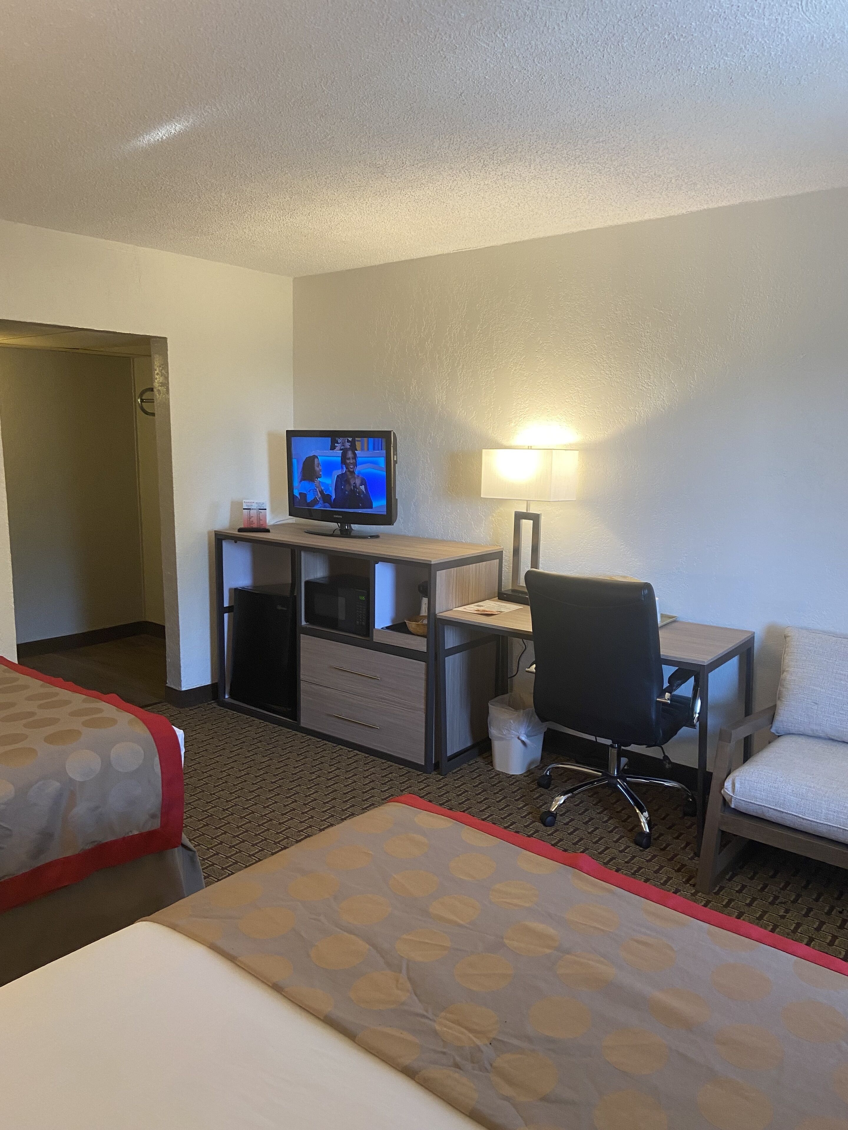 Een hotelkamer met een bed, een bureau met een computer, een stoel, een televisie en een lamp.