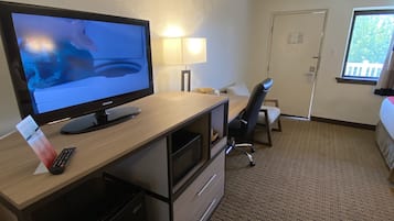 Een hotelkamer met een bureau, een televisie, een lamp, een stoel, een bed en een raam.