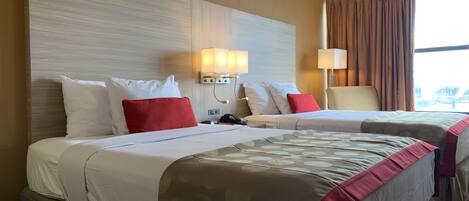 Una habitación de hotel con dos camas, un ventanal con cortinas y lámparas de pared.