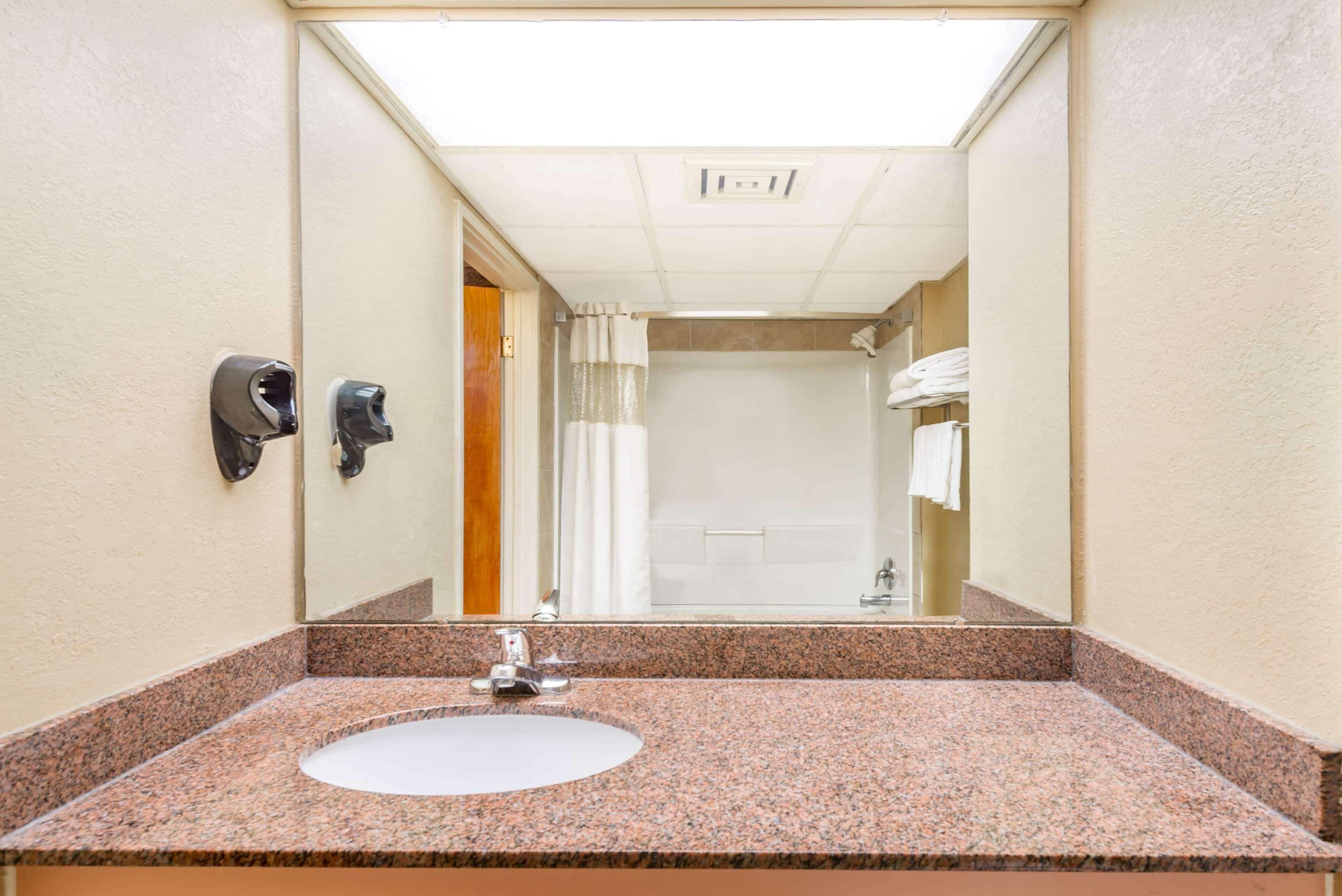 A bathroom with a granite countertop sink, a mirror, a towel rack, and a shower with a curtain.