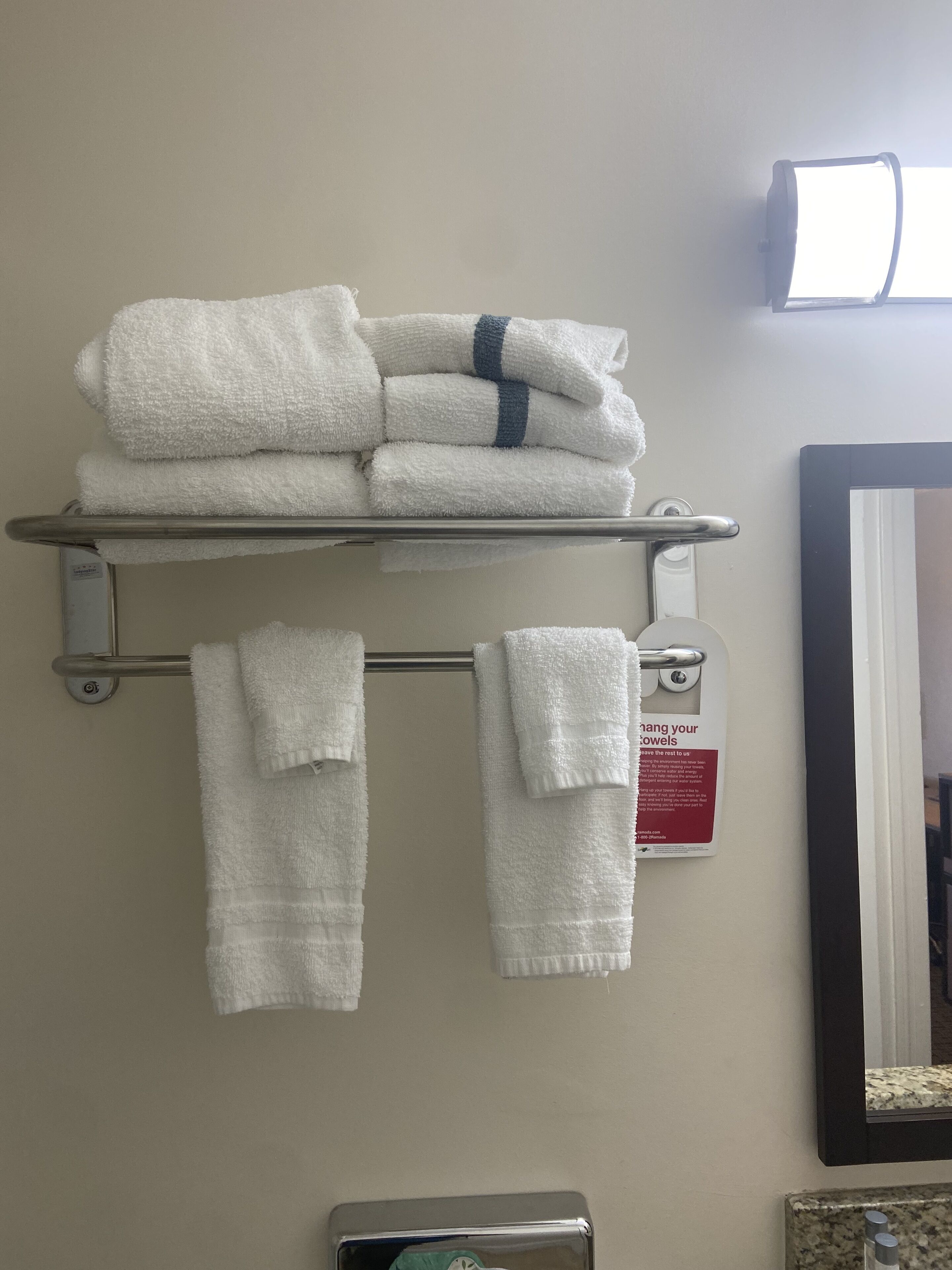 Une salle de bain avec un porte-serviettes où sont pliées les serviettes, ainsi qu’un panneau indiquant les consignes d’utilisation des serviettes.