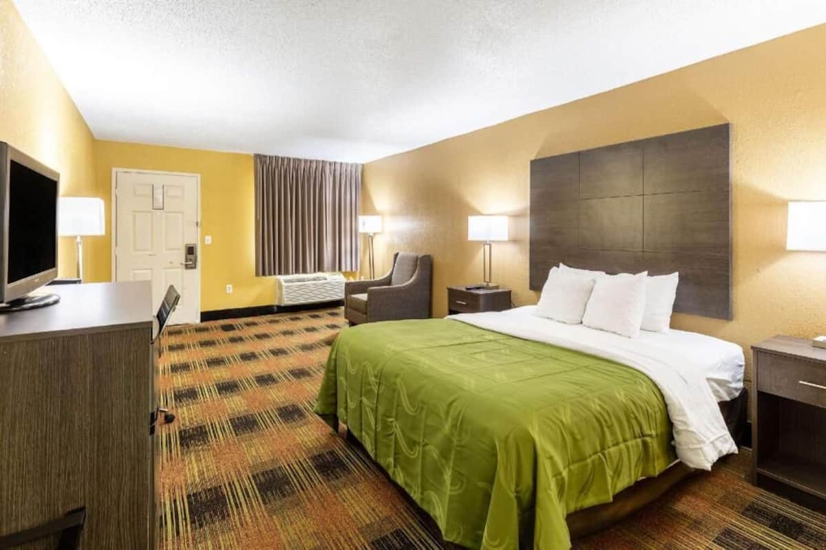 Ein Hotelzimmer mit einem Bett, einem Schreibtisch, einem Stuhl, einem Fernseher und einer Lampe.