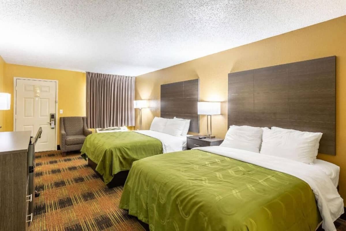 Ein Hotelzimmer mit zwei Betten, einem Schreibtisch, einem Stuhl und einer Tür.