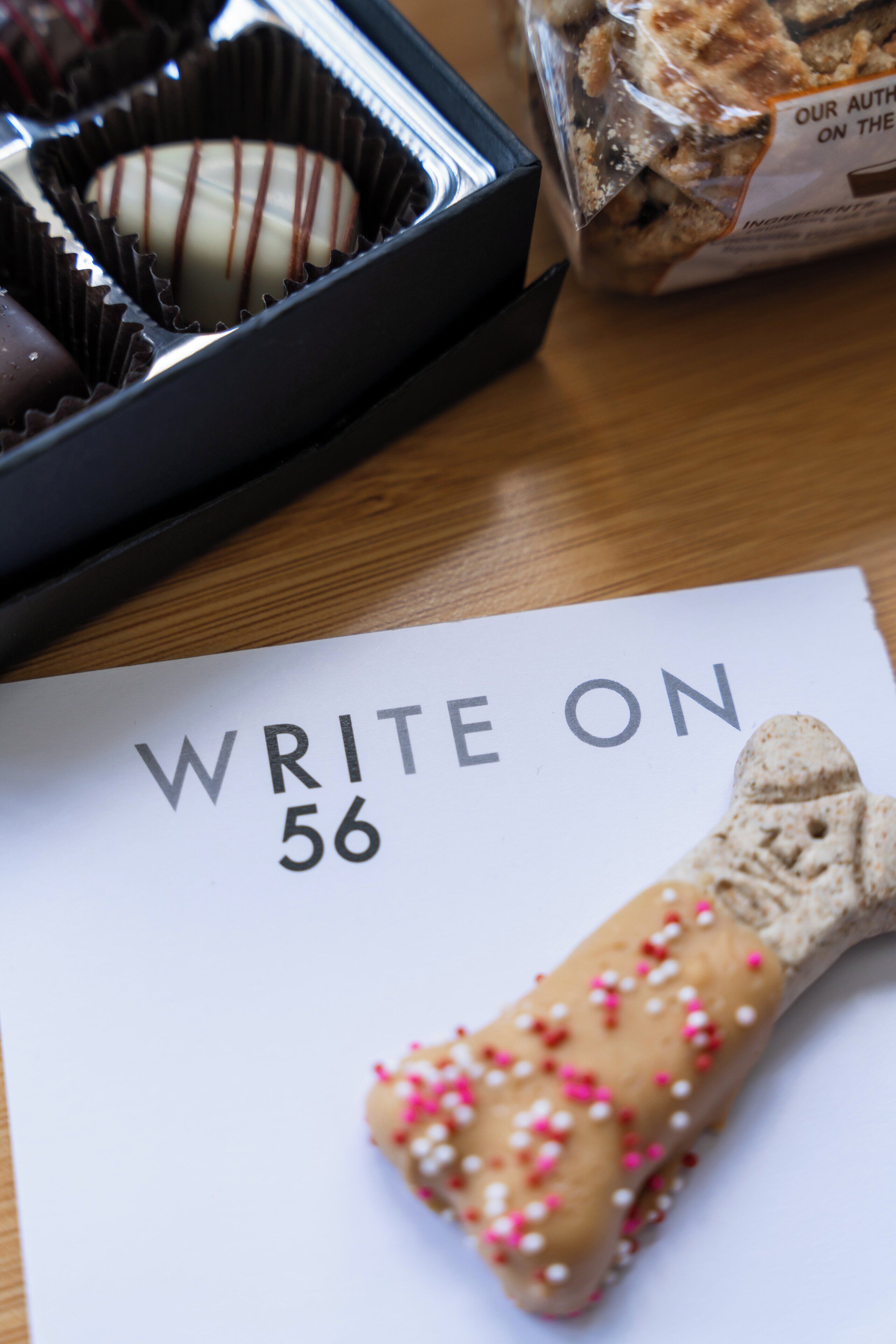 A piece of paper with "WRITE ON 56" and a bone-shaped cookie with pink and white sprinkles.