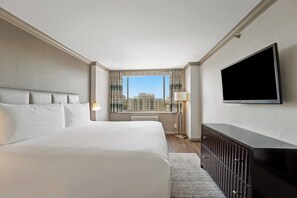 A hotel room with a large bed, a flat-screen TV, a desk, and a window with a city view.