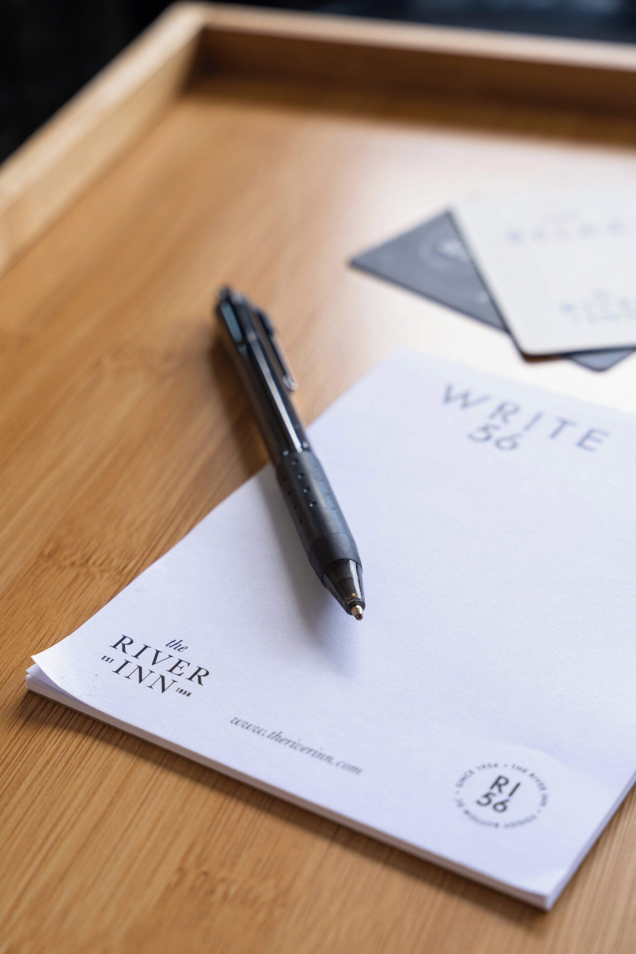 A pen on a white paper with "WRITE" and "the RIVER INN" text, placed on a wooden tray.