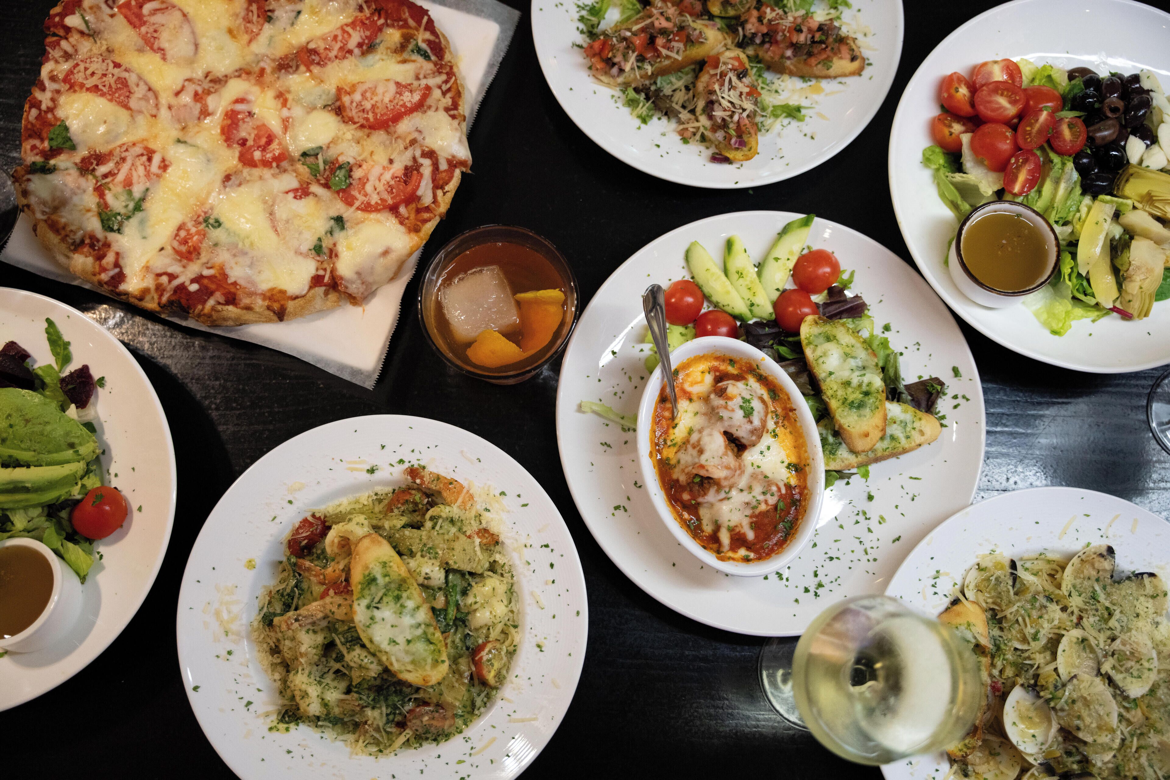 Diverse gerechten, waaronder pizza, salades en pasta, wat een eetgelegenheid doet vermoeden.