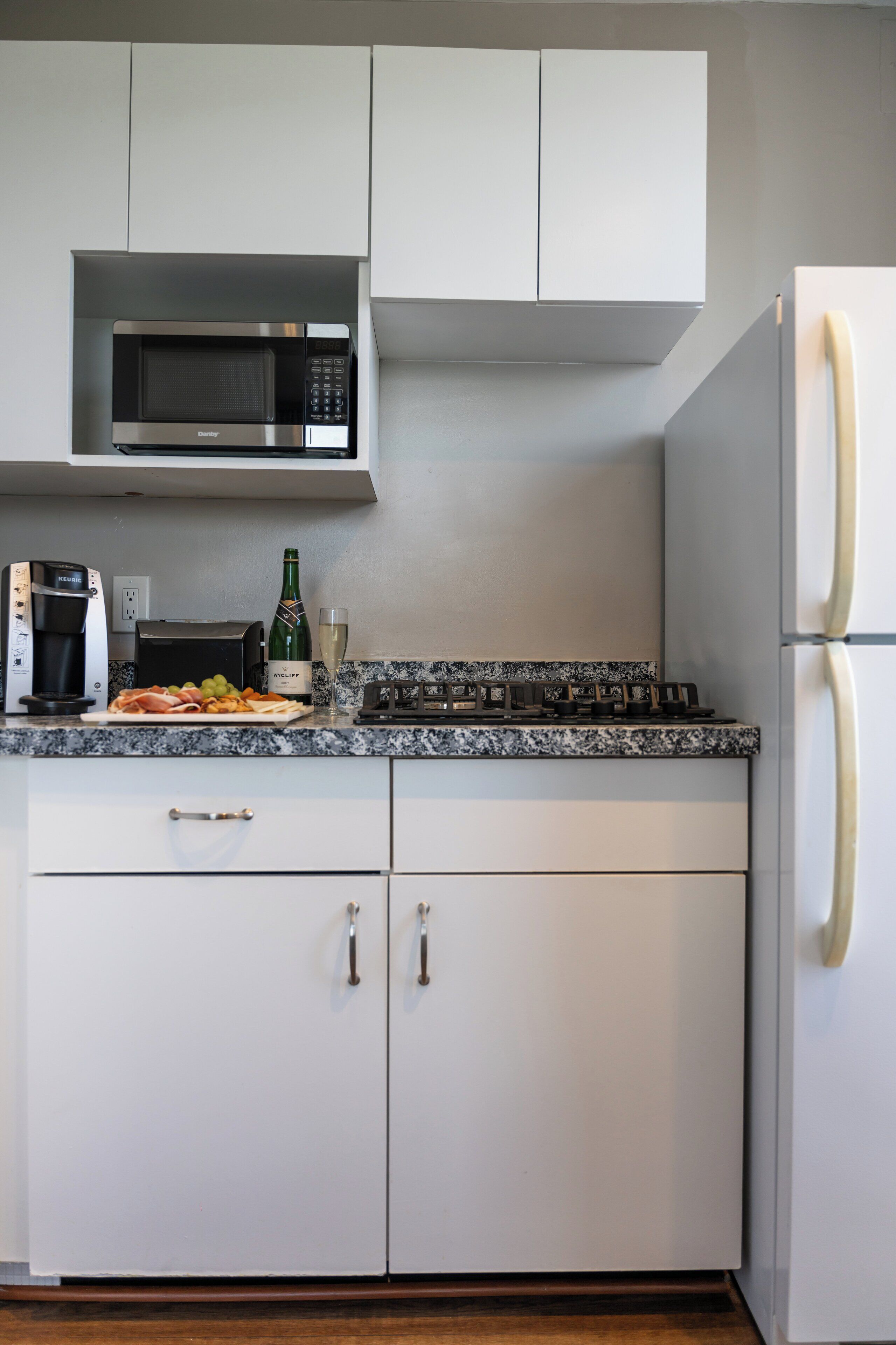 A modern kitchen with white cabinets, a built-in microwave, a gas stove, and a refrigerator.