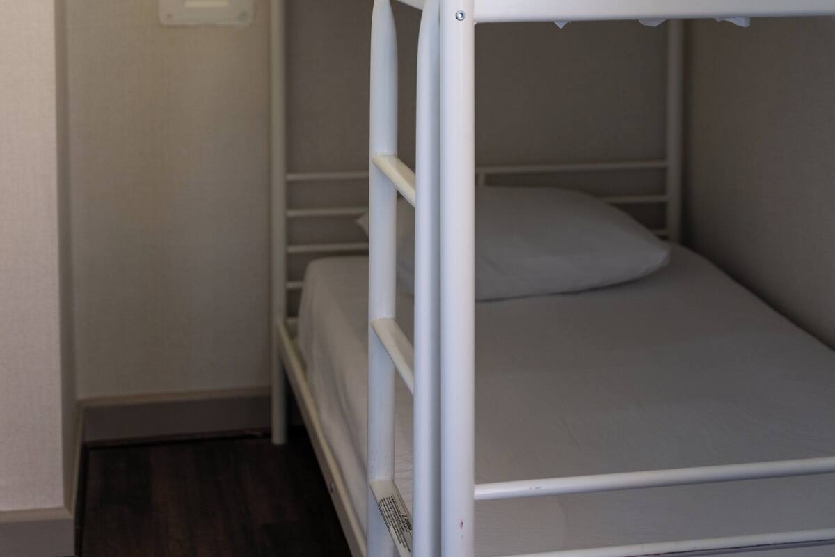 A bunk bed with white bedding and a white metal frame.