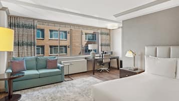 Quarto de hotel moderno com cama, escrivaninha, sofá e vista para a paisagem urbana.