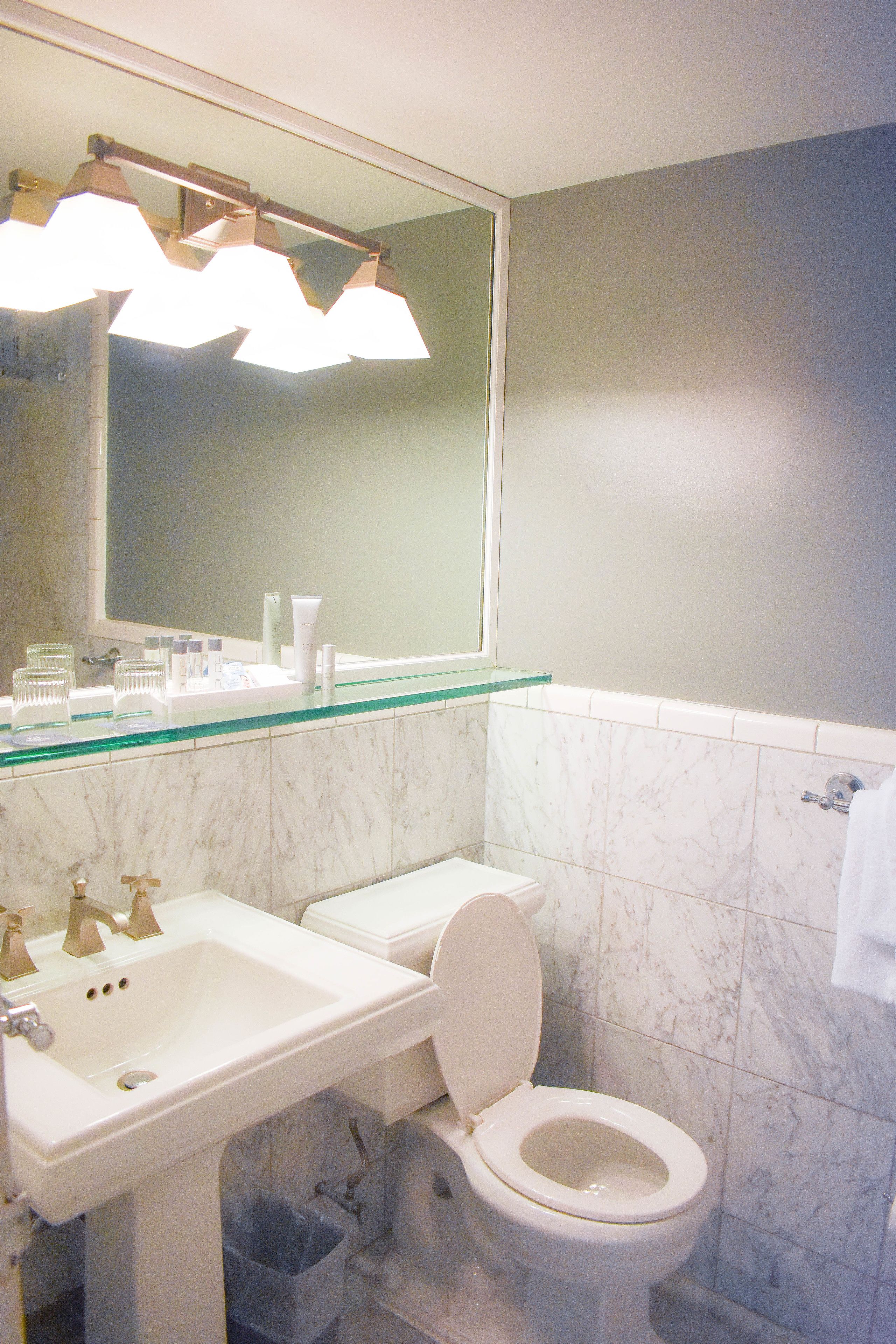 A bathroom with a white sink, toilet, and a glass shelf above the sink.