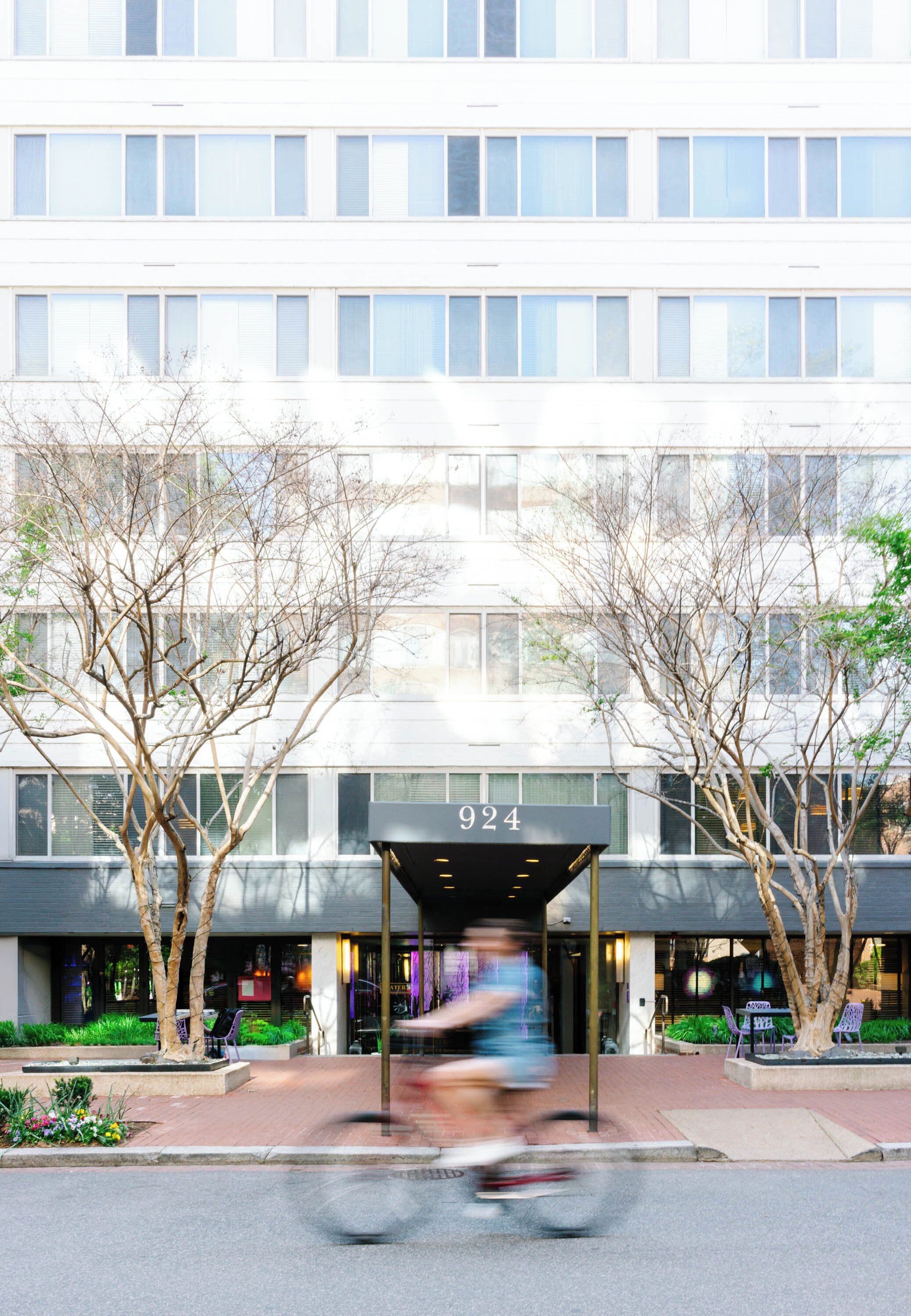 A modern building with a covered entrance, numbered 924, and a landscaped area with trees and benches.
