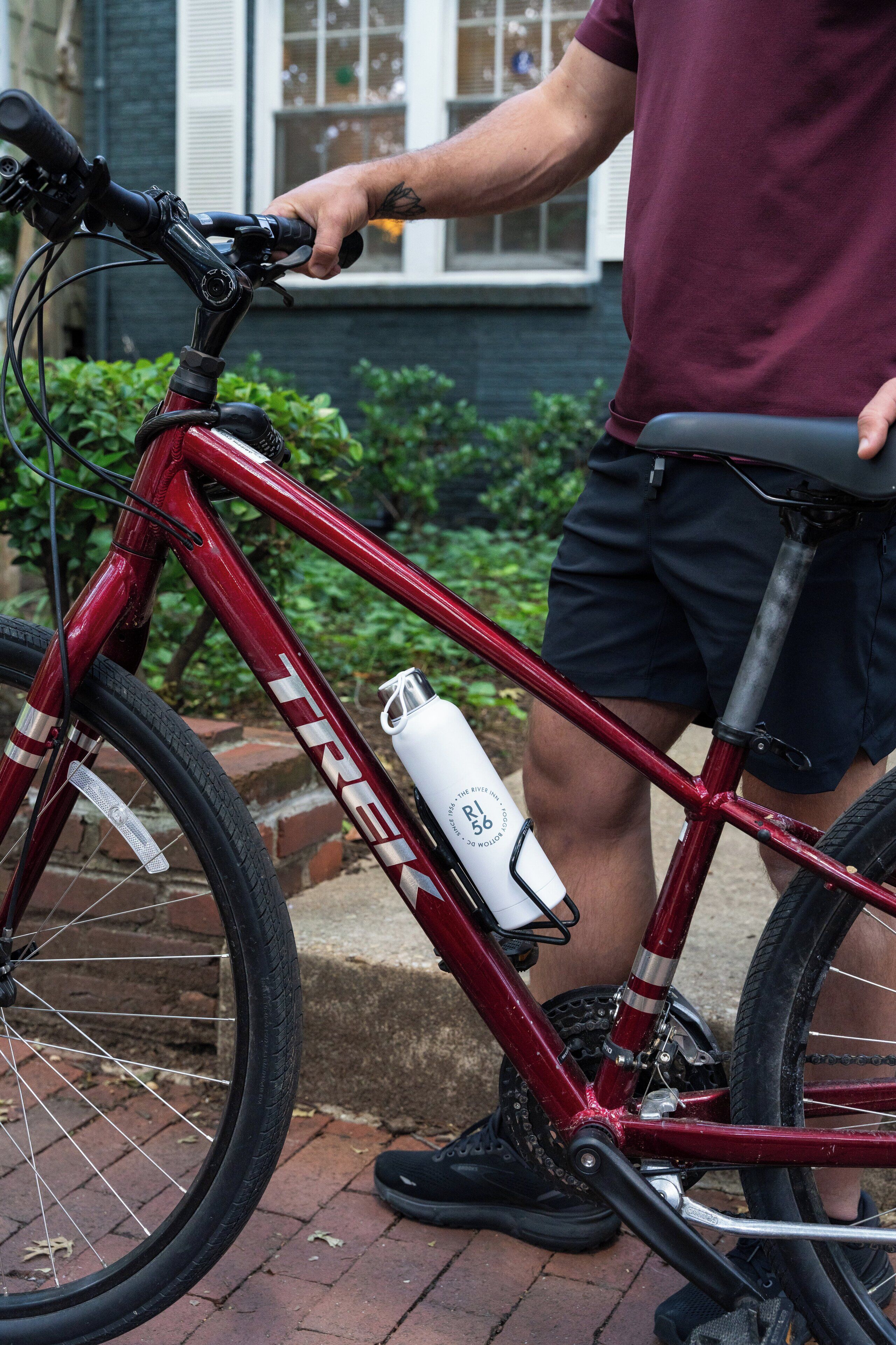 Una bicicleta roja con una botella de agua sujeta al cuadro, estacionada sobre una superficie de ladrillo.