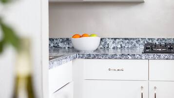 A kitchen with a white countertop, a bowl of fruit, a microwave, and a stove.