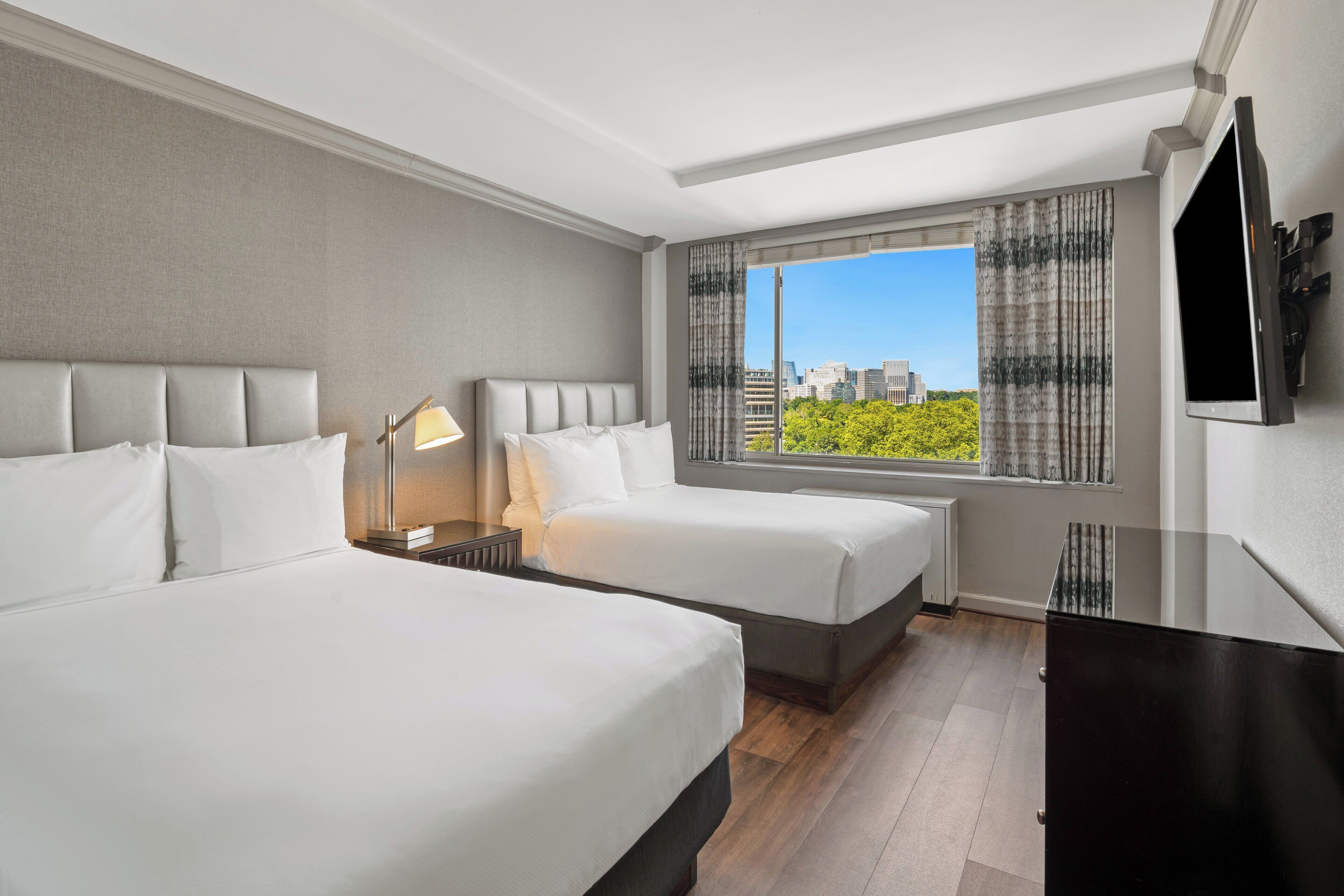 Habitación de hotel con dos camas, televisión, escritorio y ventana con vistas a la ciudad.